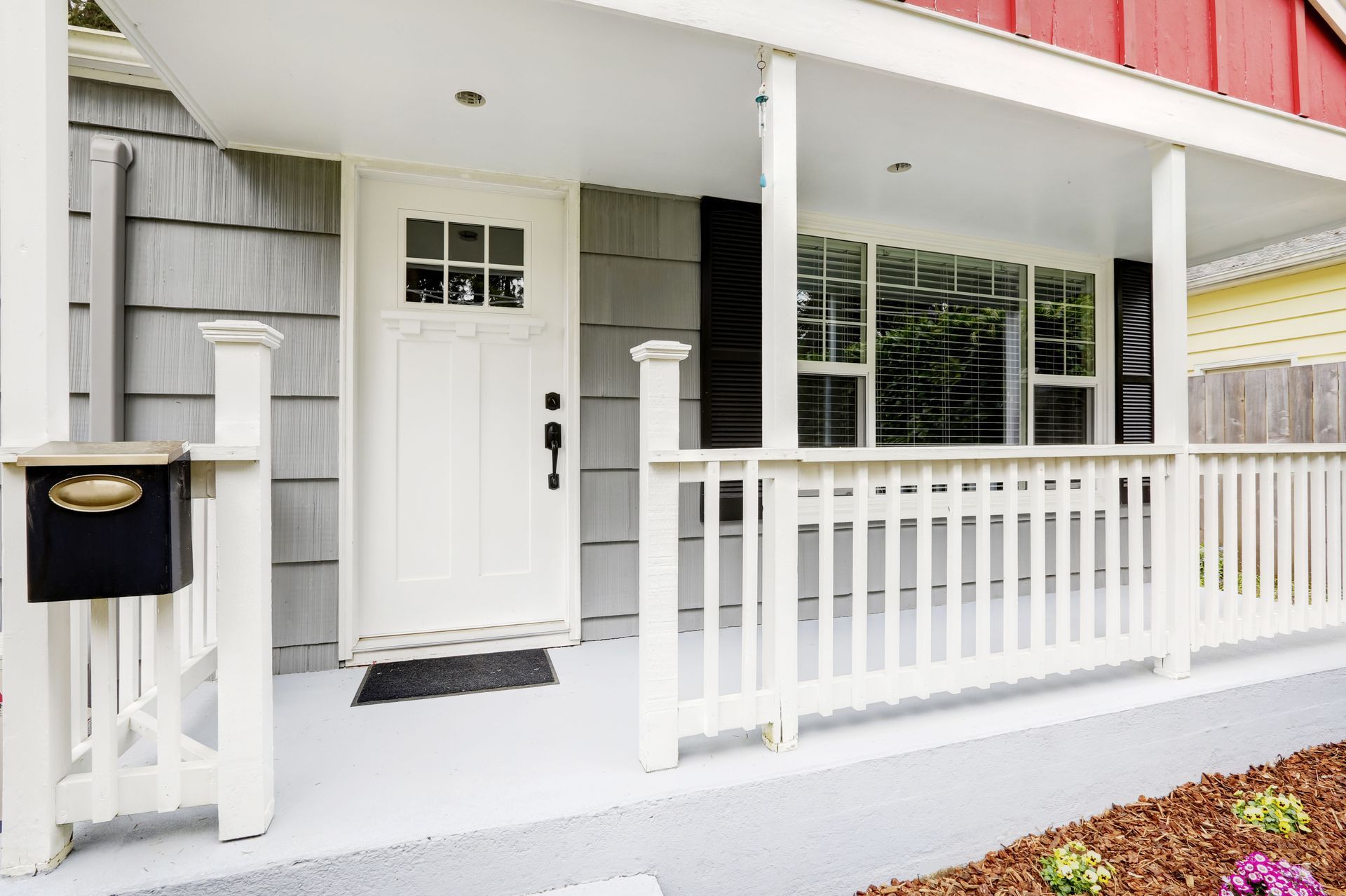 White front porch with a white door, mailbox, and railing. Gray siding. Red roof.