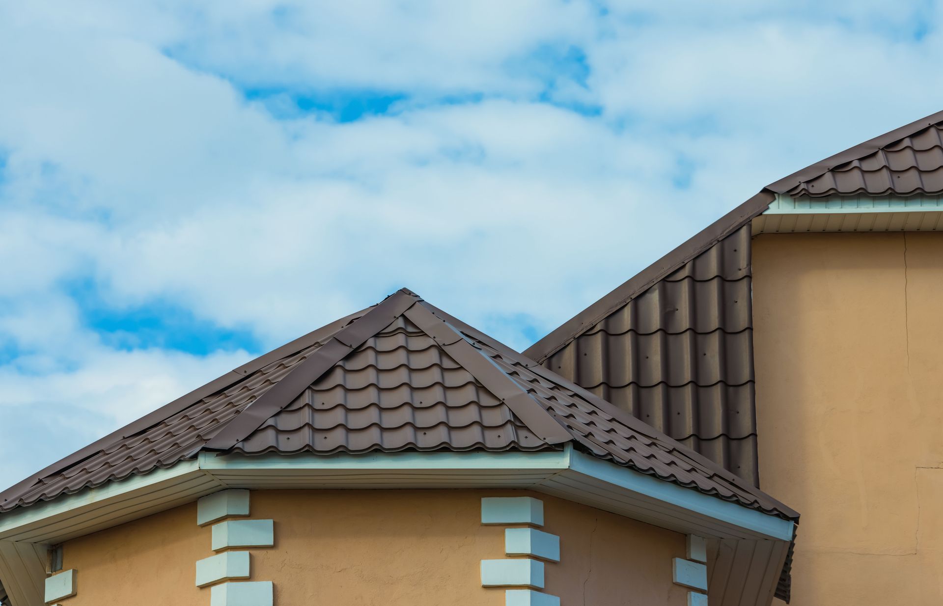 Brown tile roof on a tan building with a blue and cloudy sky in the background.