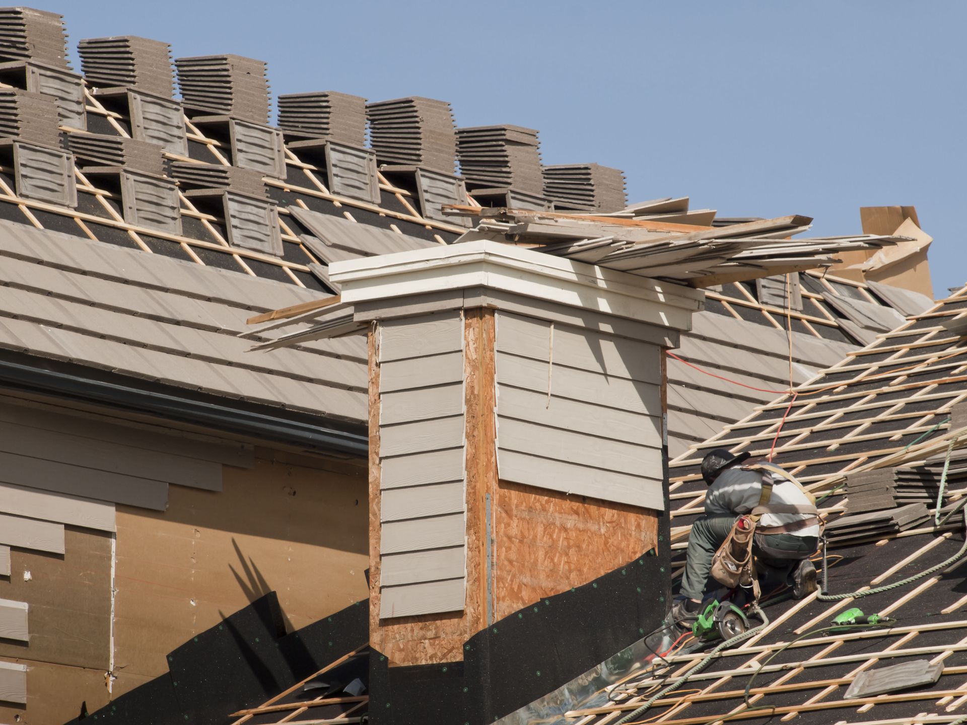 Roofers installing tiles on a residential roof, with chimney visible.