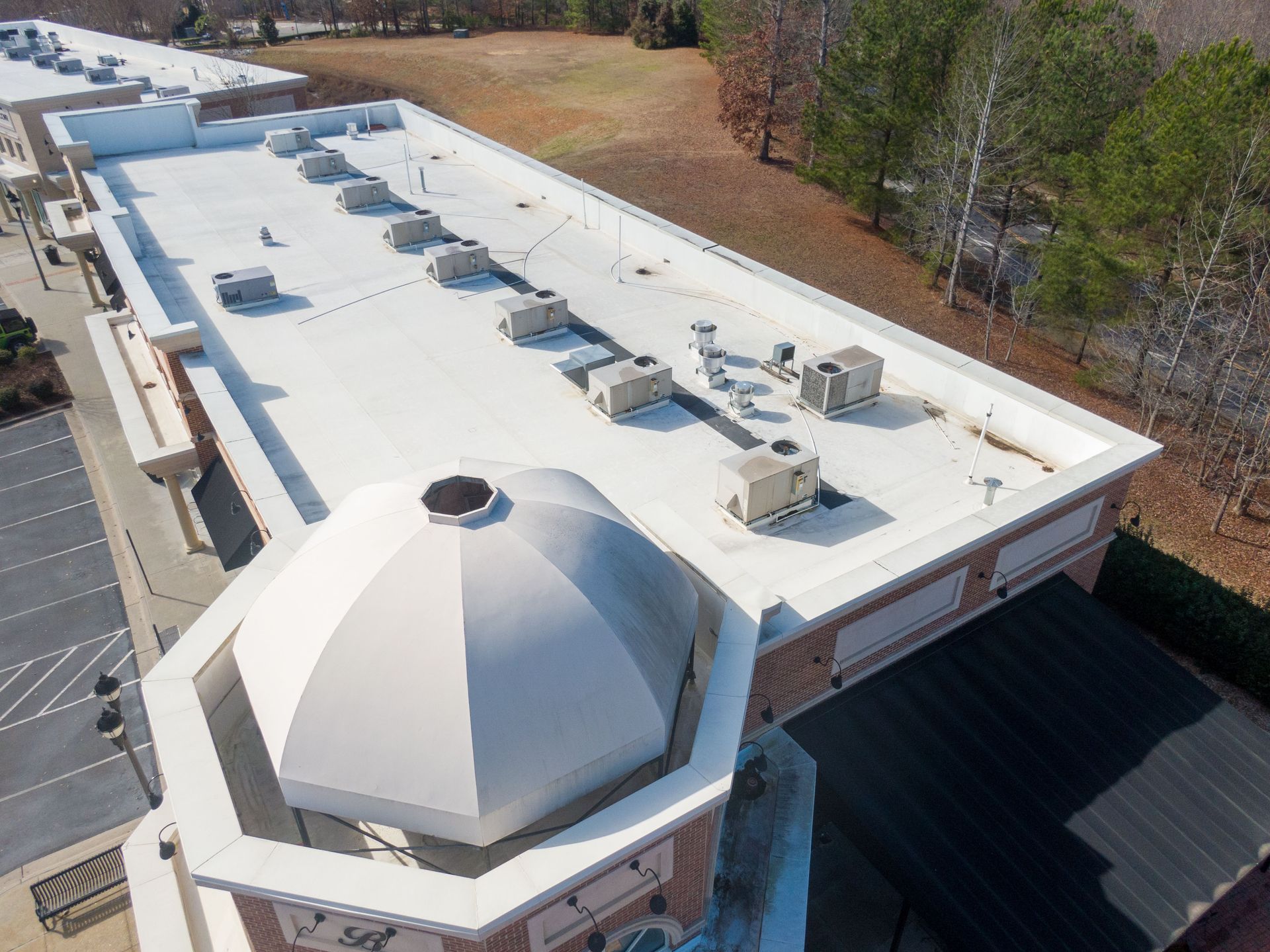 Overhead view of a building with a white flat roof, air conditioning units, and a domed section.
