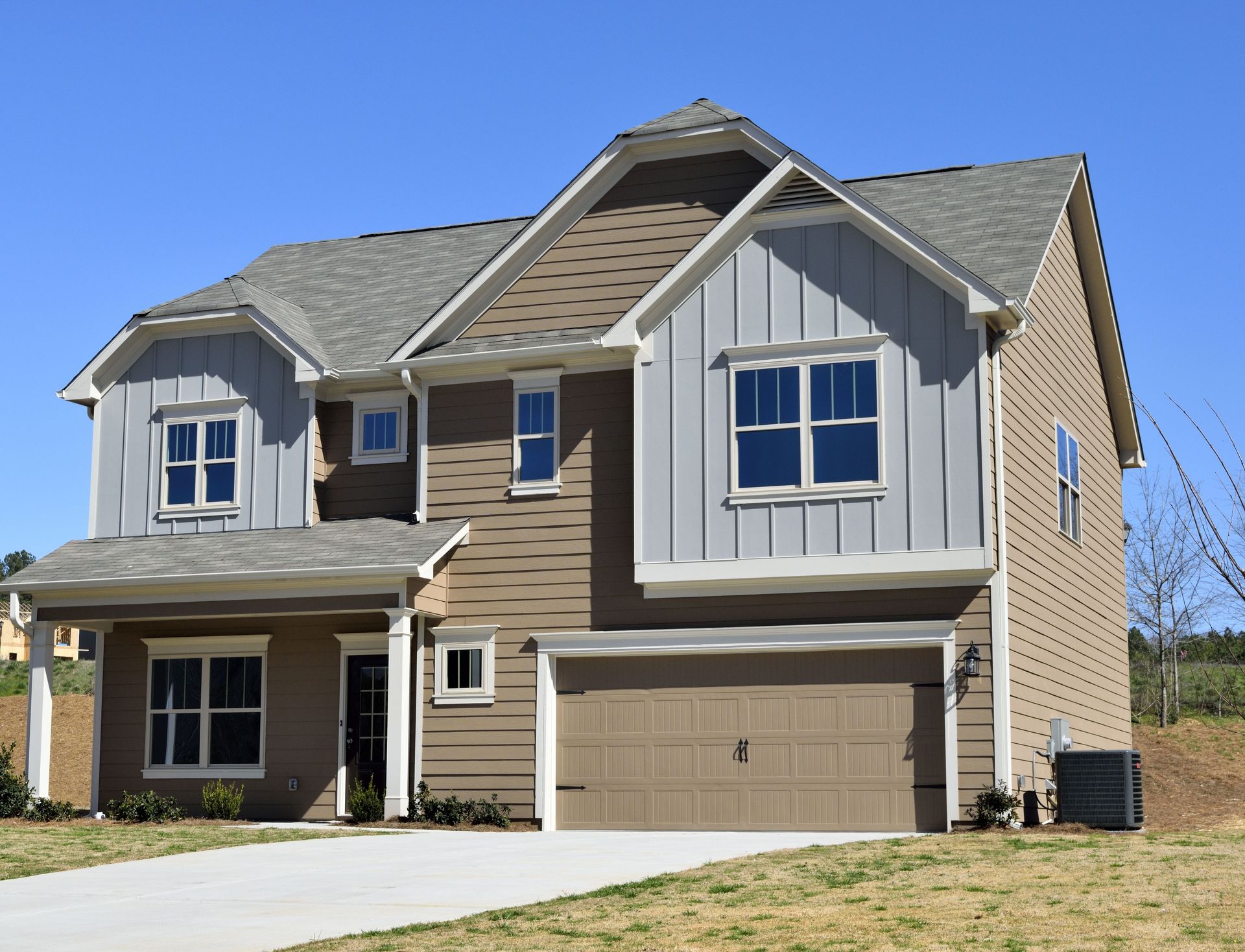 Two-story house with brown and gray siding, attached garage, and a concrete driveway on a sunny day.