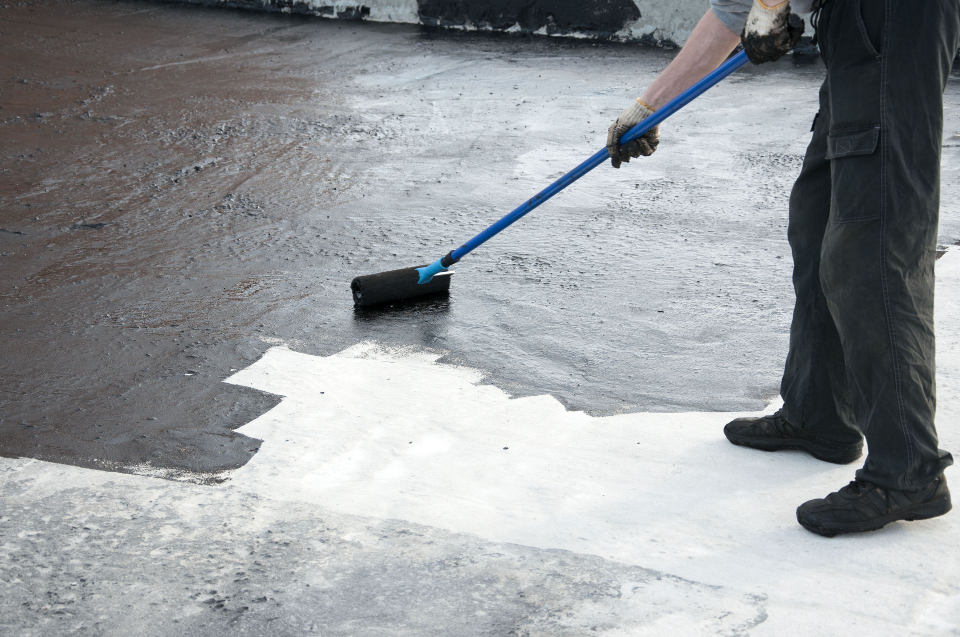 Person using a roller to apply black sealant on a white roof, covering the surface.