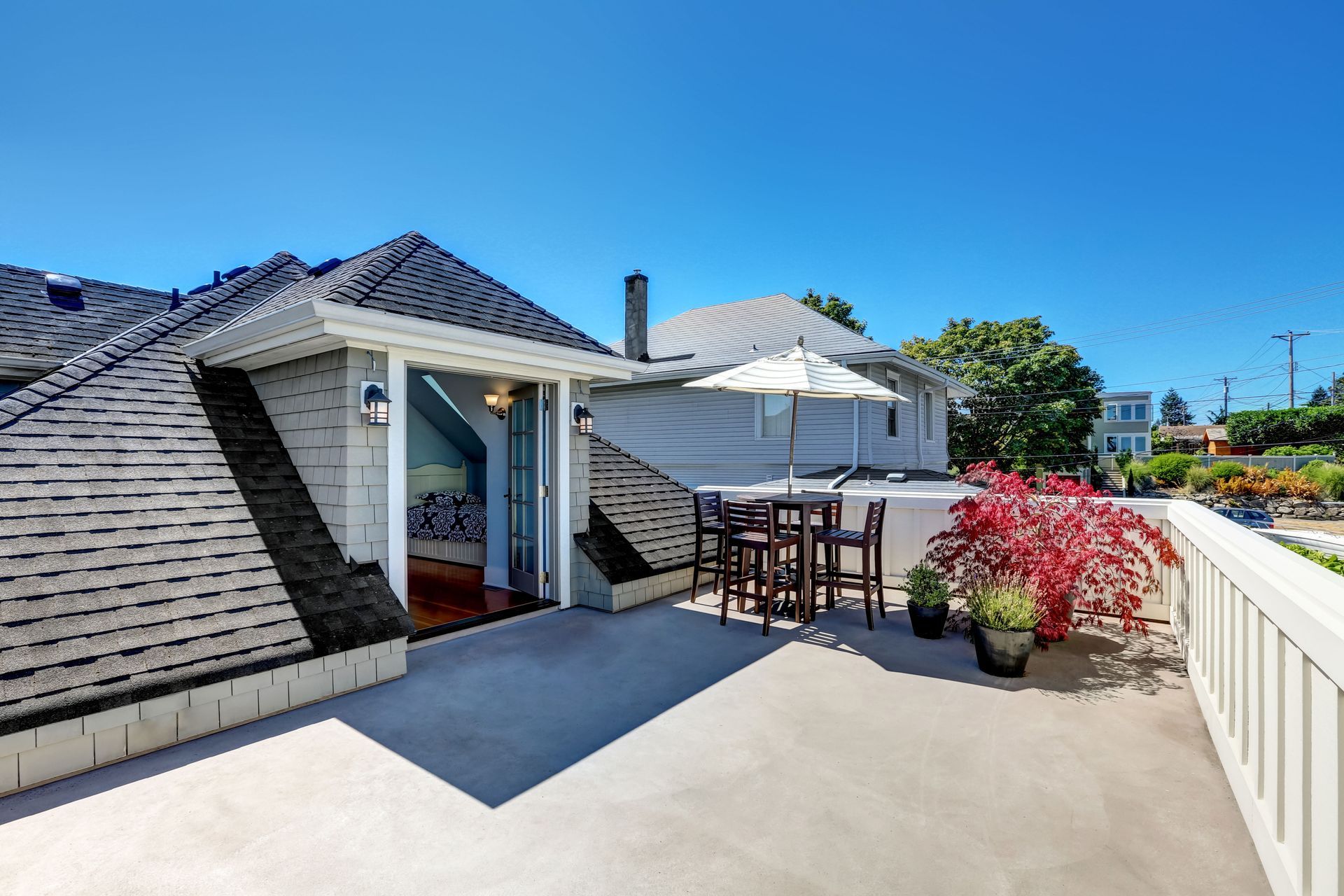 Rooftop deck with table, umbrella, and potted plants, accessed through a door. Clear blue sky overhead.
