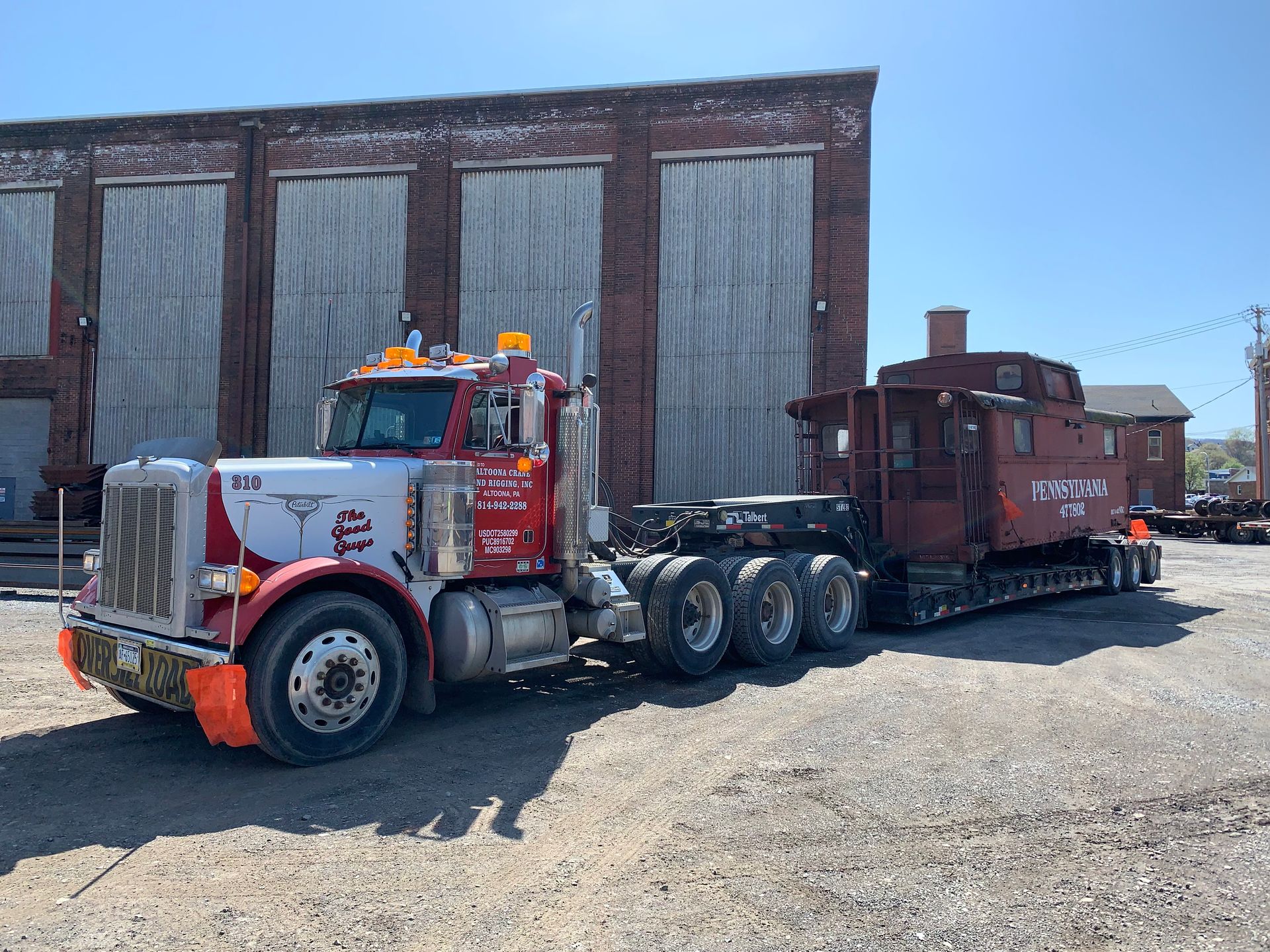 Two semi trucks parked beside a weathered warehouse on a sunny day