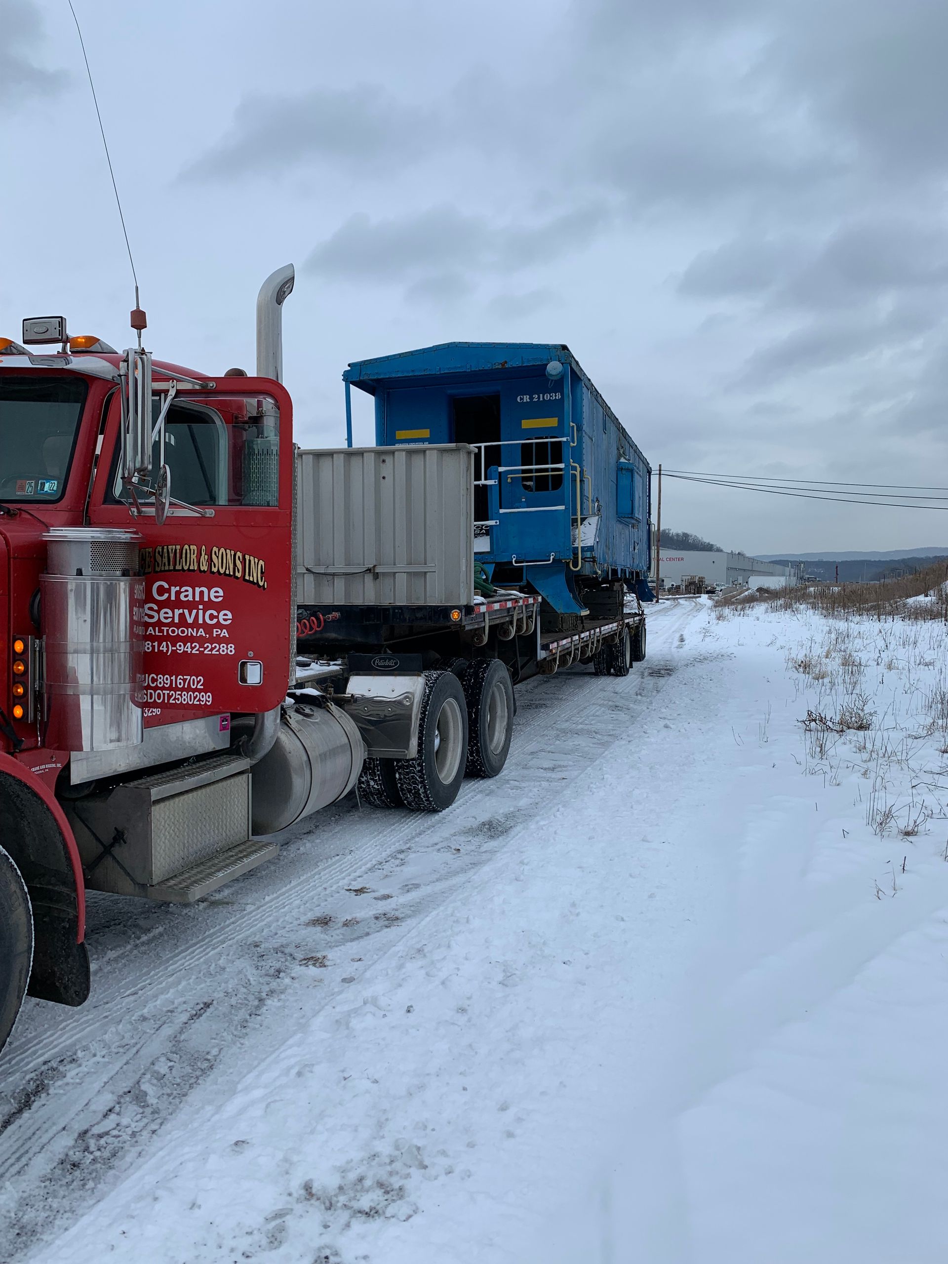 Red truck hauling a blue trailer on a snowy road under an overcast sky