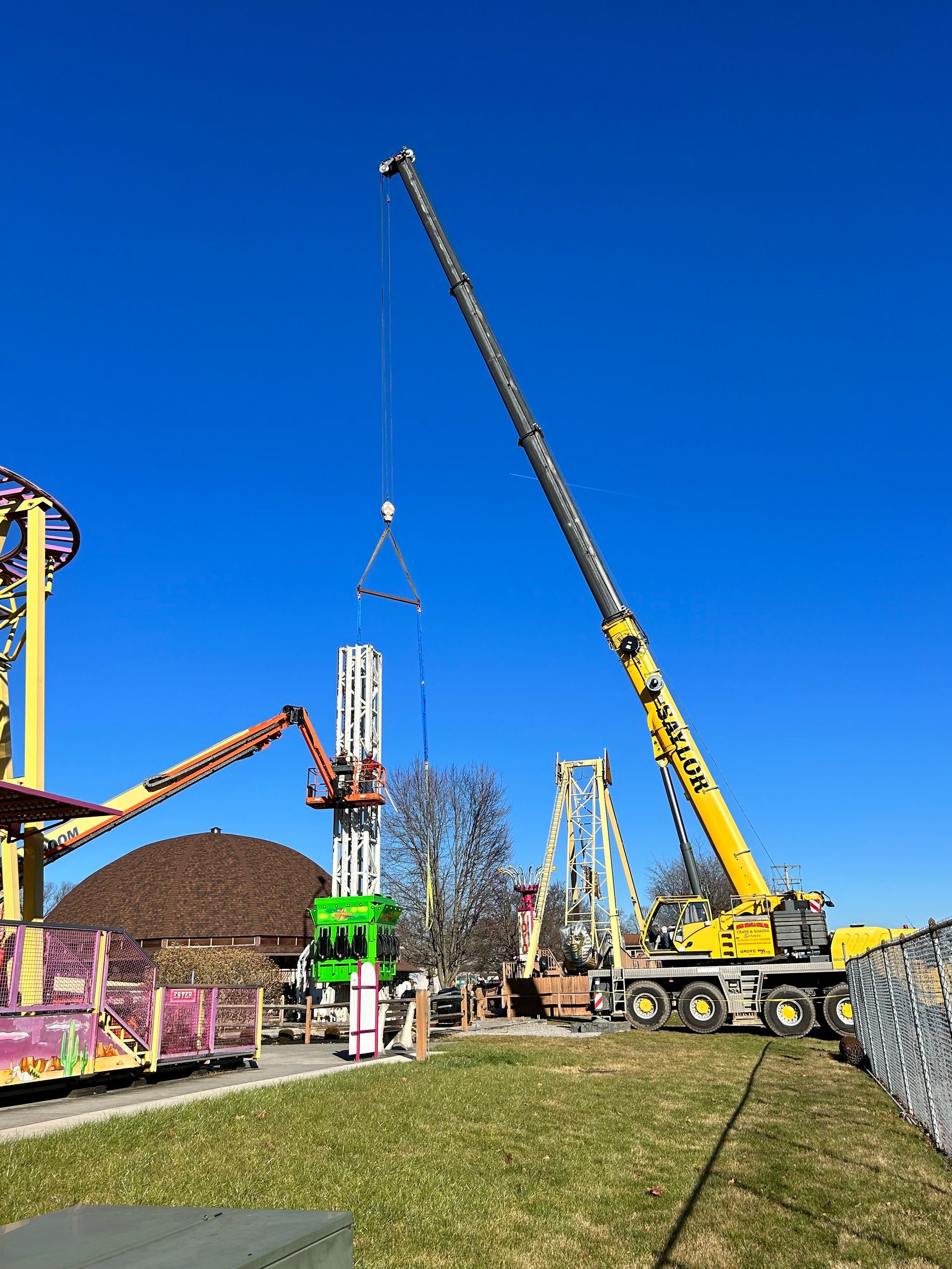 Construction site with yellow crane lifting a tall white panel under a bright blue sky