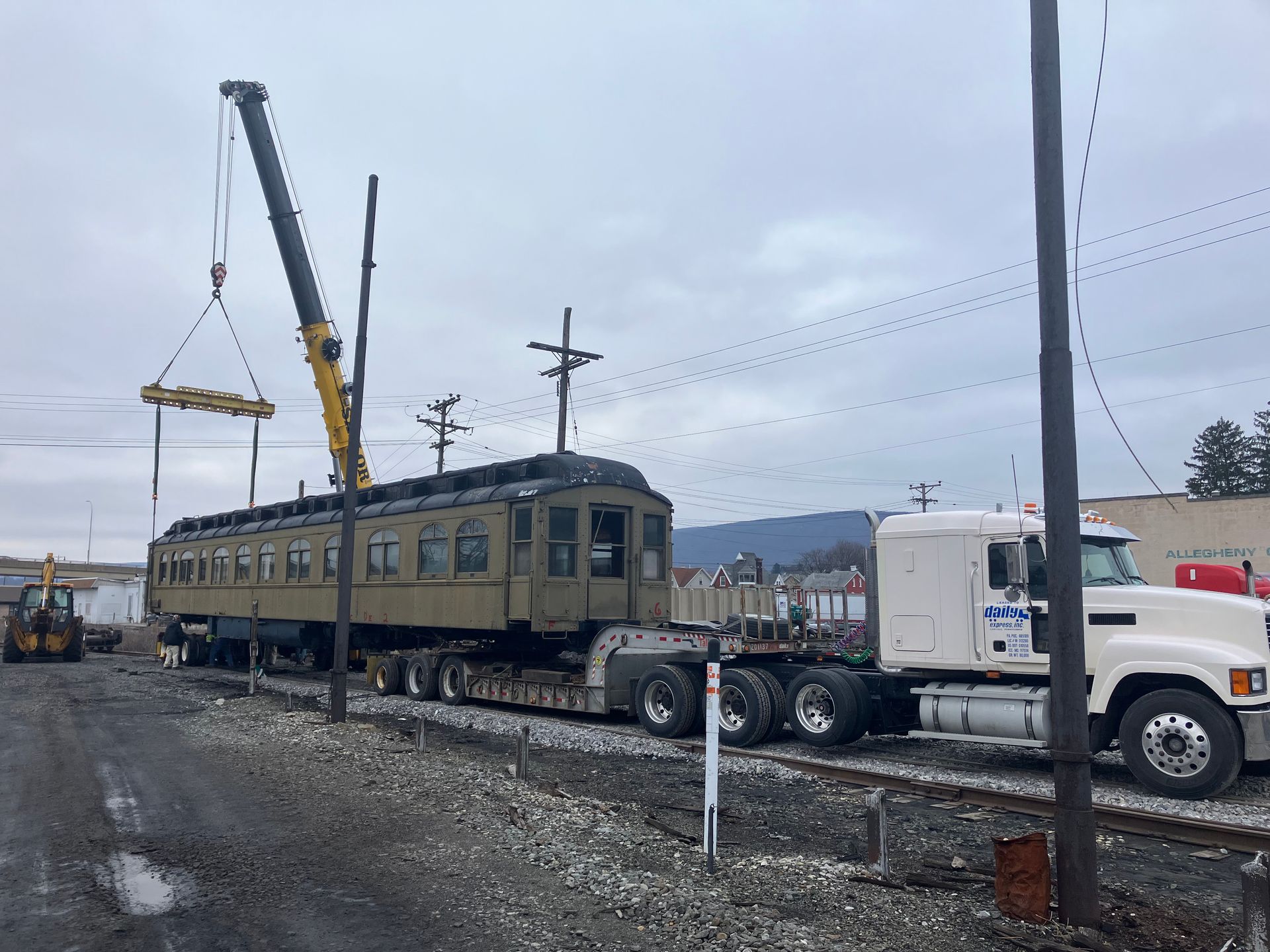 Crane loading a vintage railcar onto a flatbed truck in a rail yard.