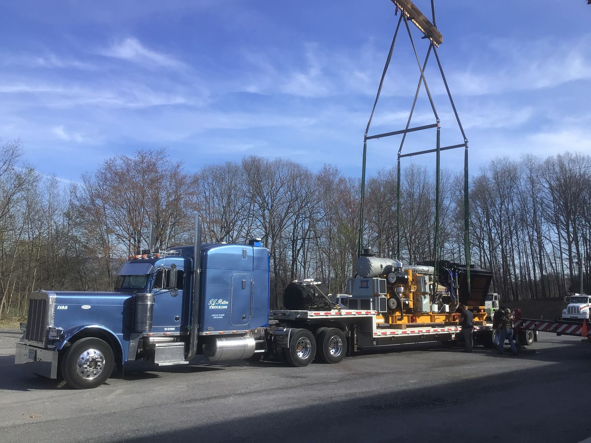 Blue semi truck hauling a large metal frame on a flatbed trailer along a roadside.