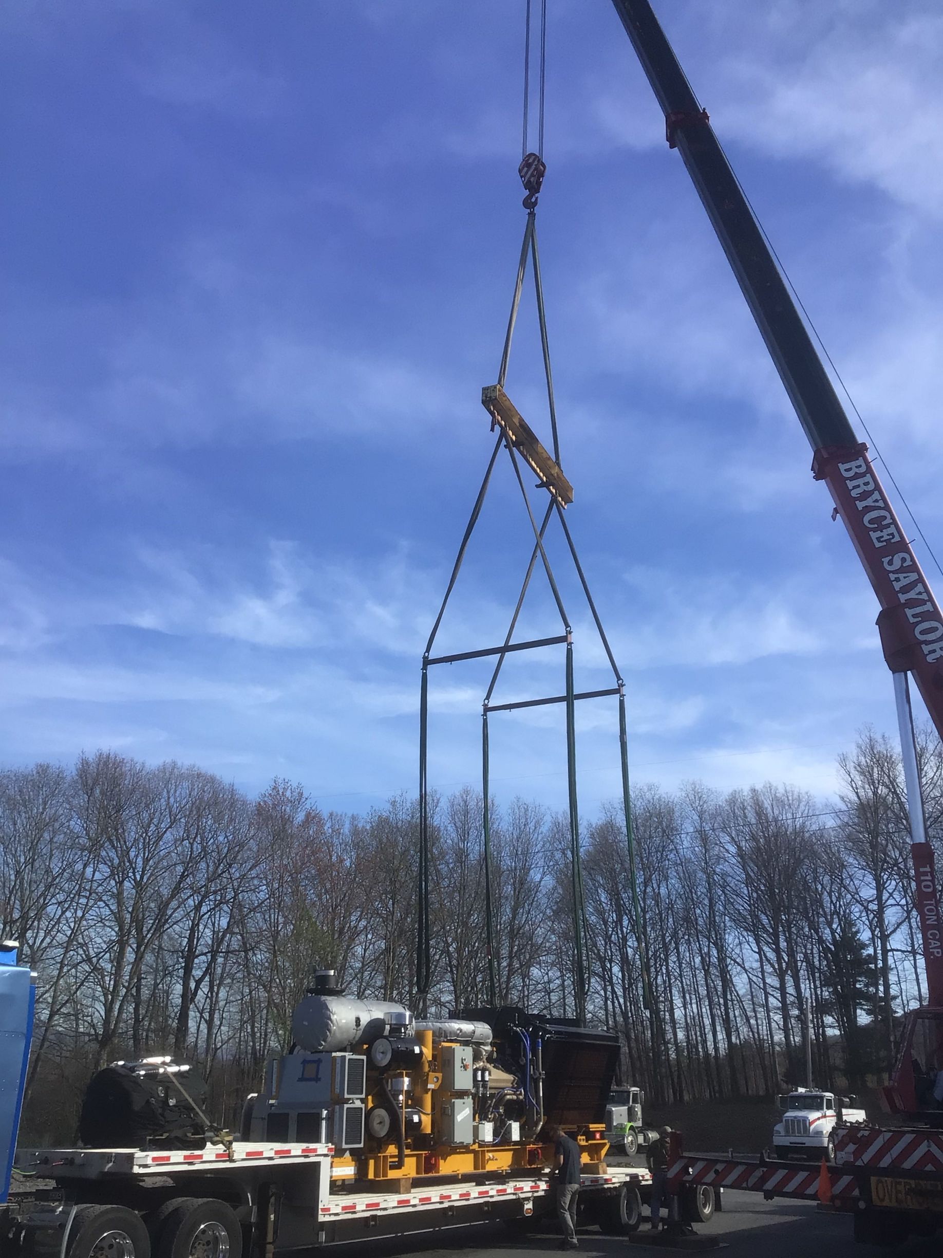 Crane lifting a large metal frame at an outdoor worksite under a blue sky.