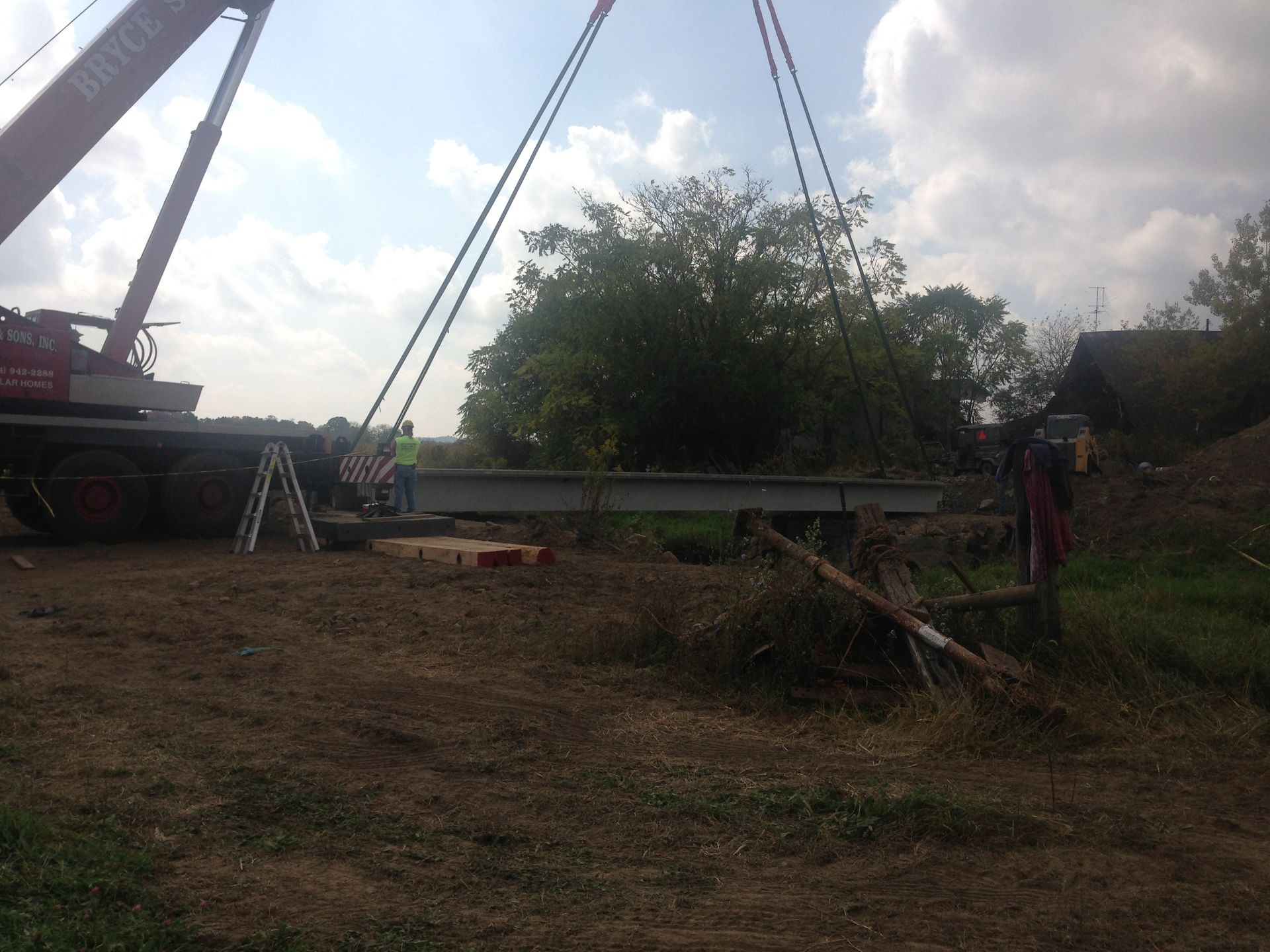 Crane lifting a fallen tree near a road under a cloudy sky