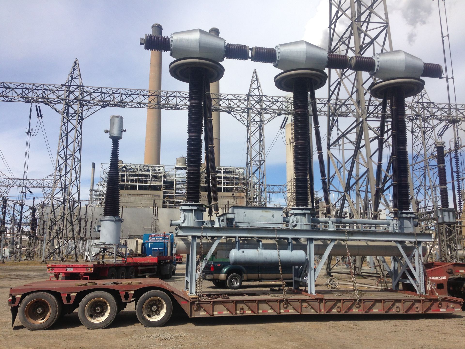 Large electrical substation with transformer equipment on a trailer under overhead power lines.