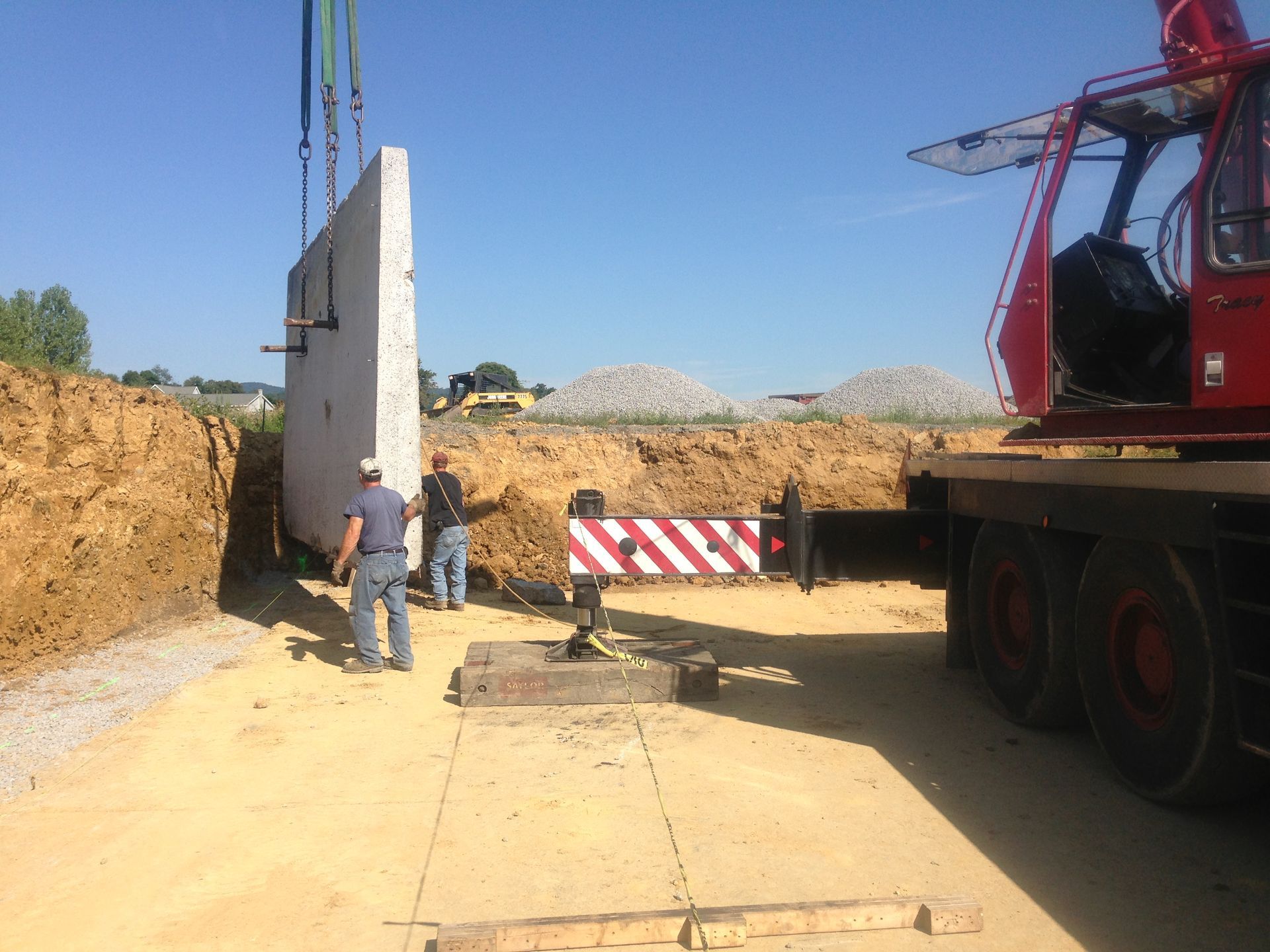 Construction site with a crane lifting a concrete wall beside a truck and a worker nearby