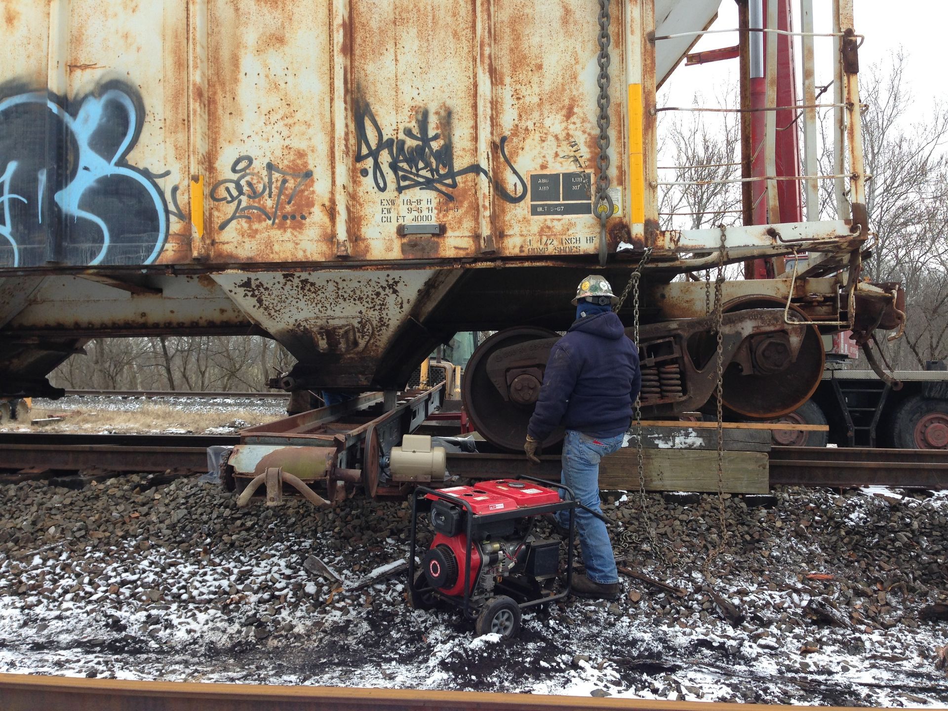 Person with dog by red generator beside rusty train car in snowy rail yard