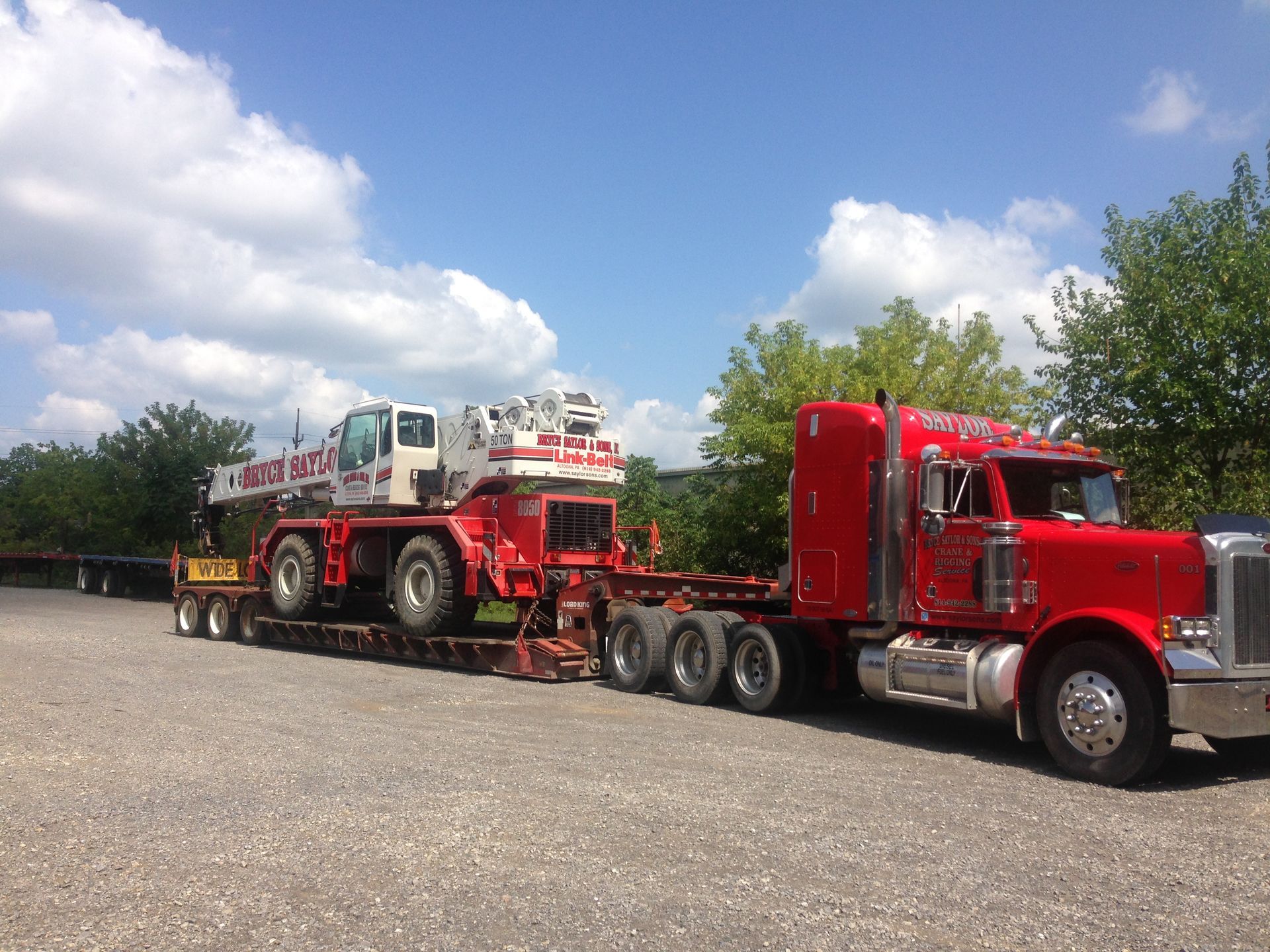 Red semi-truck hauling a heavy construction vehicle on a trailer under a blue sky.