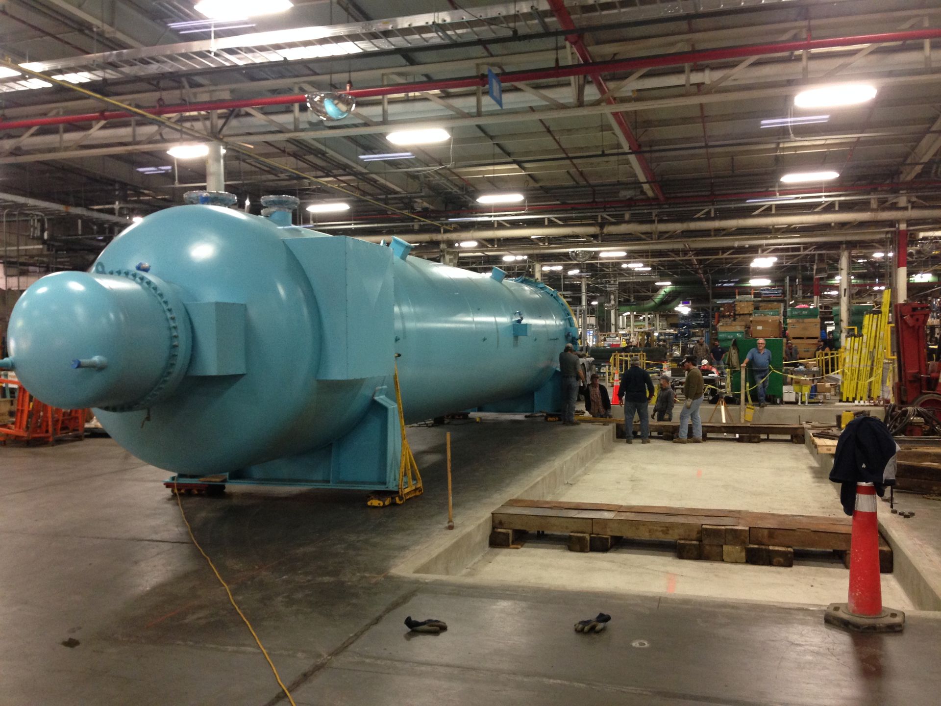 Large blue industrial tank or pressure vessel in a factory workshop, with workers and equipment nearby