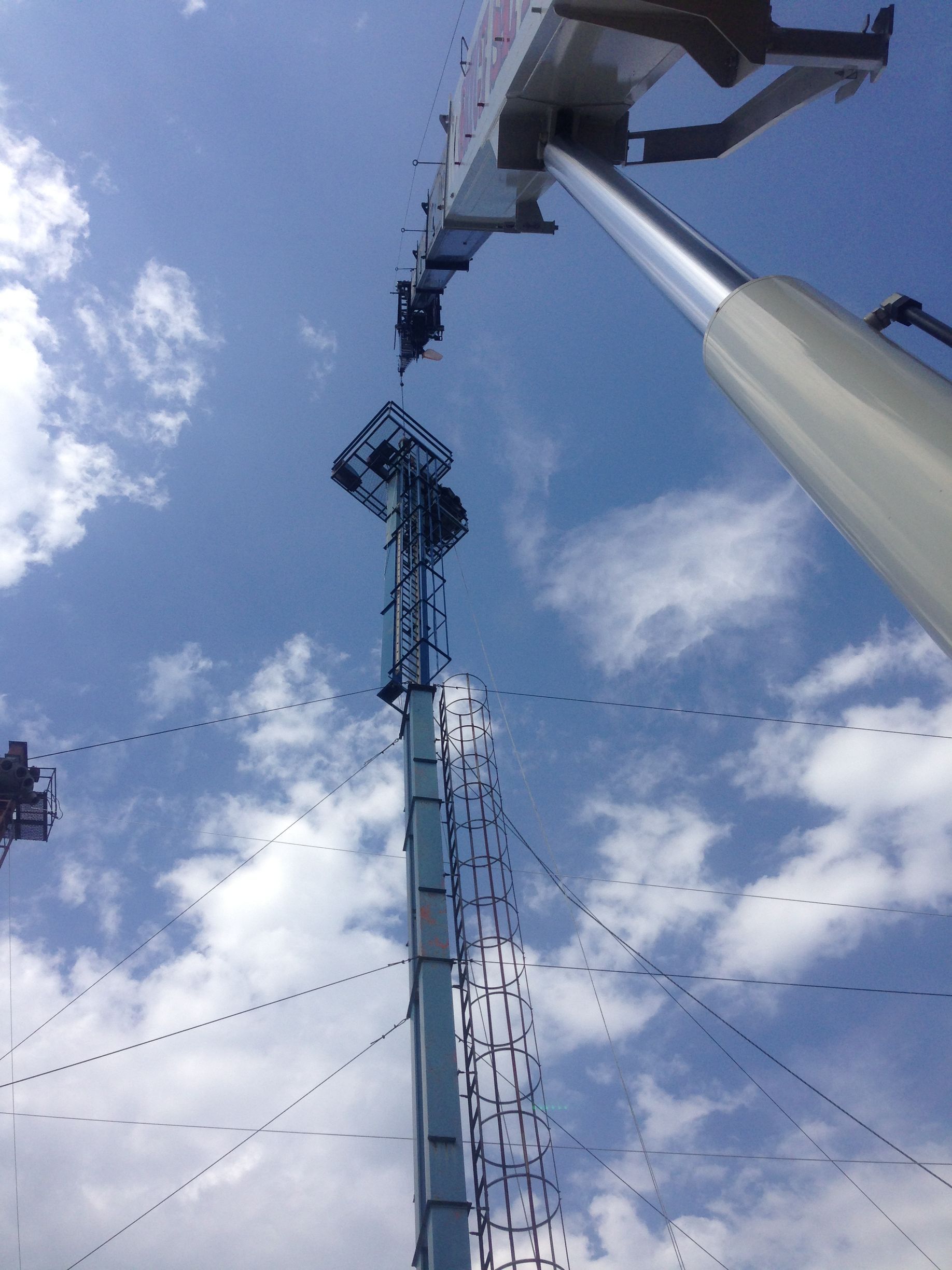 Tall metal communications tower against a blue sky with clouds, viewed from below