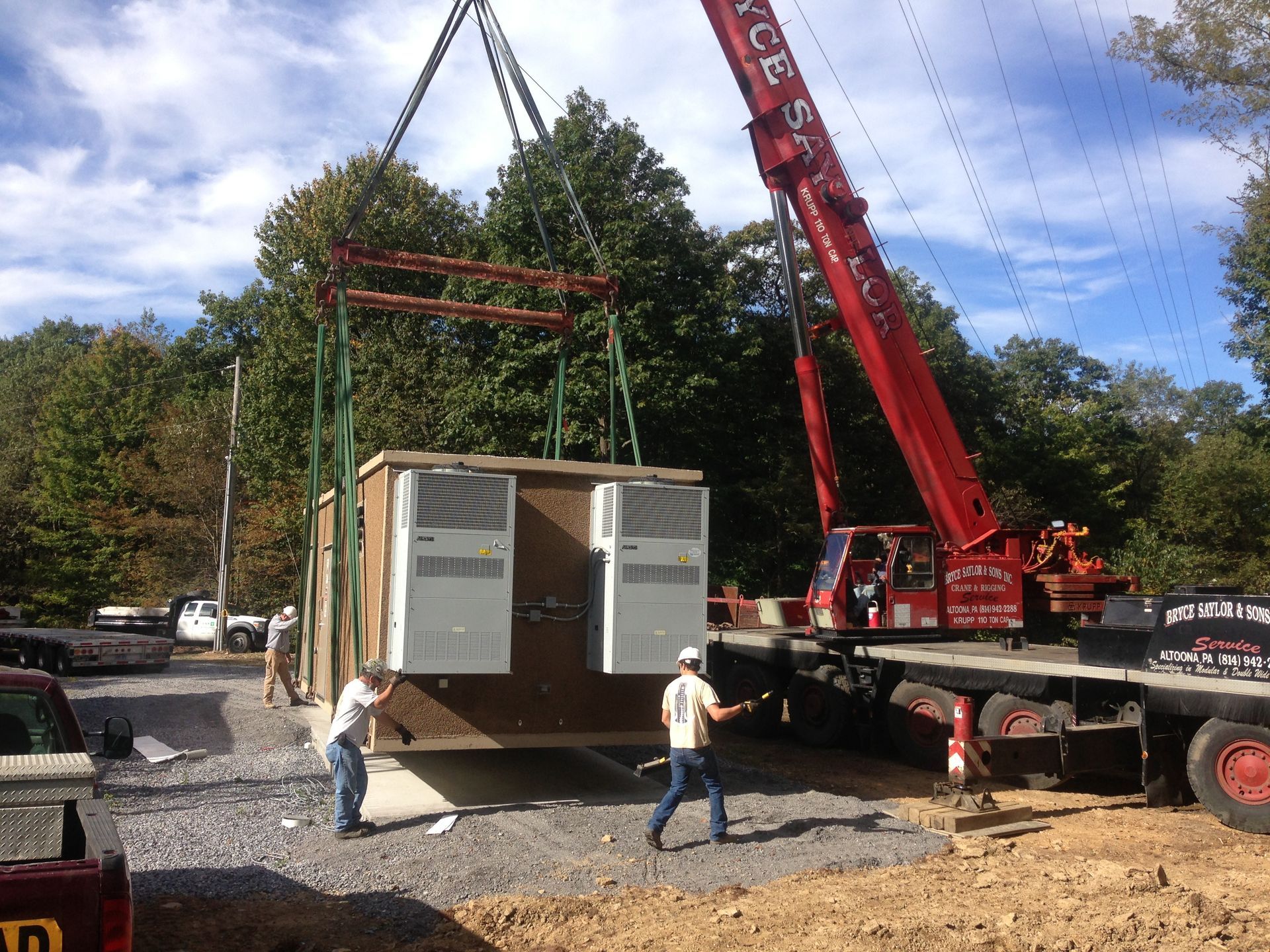 Crane lifting a wooden modular room onto a flatbed truck at a construction site