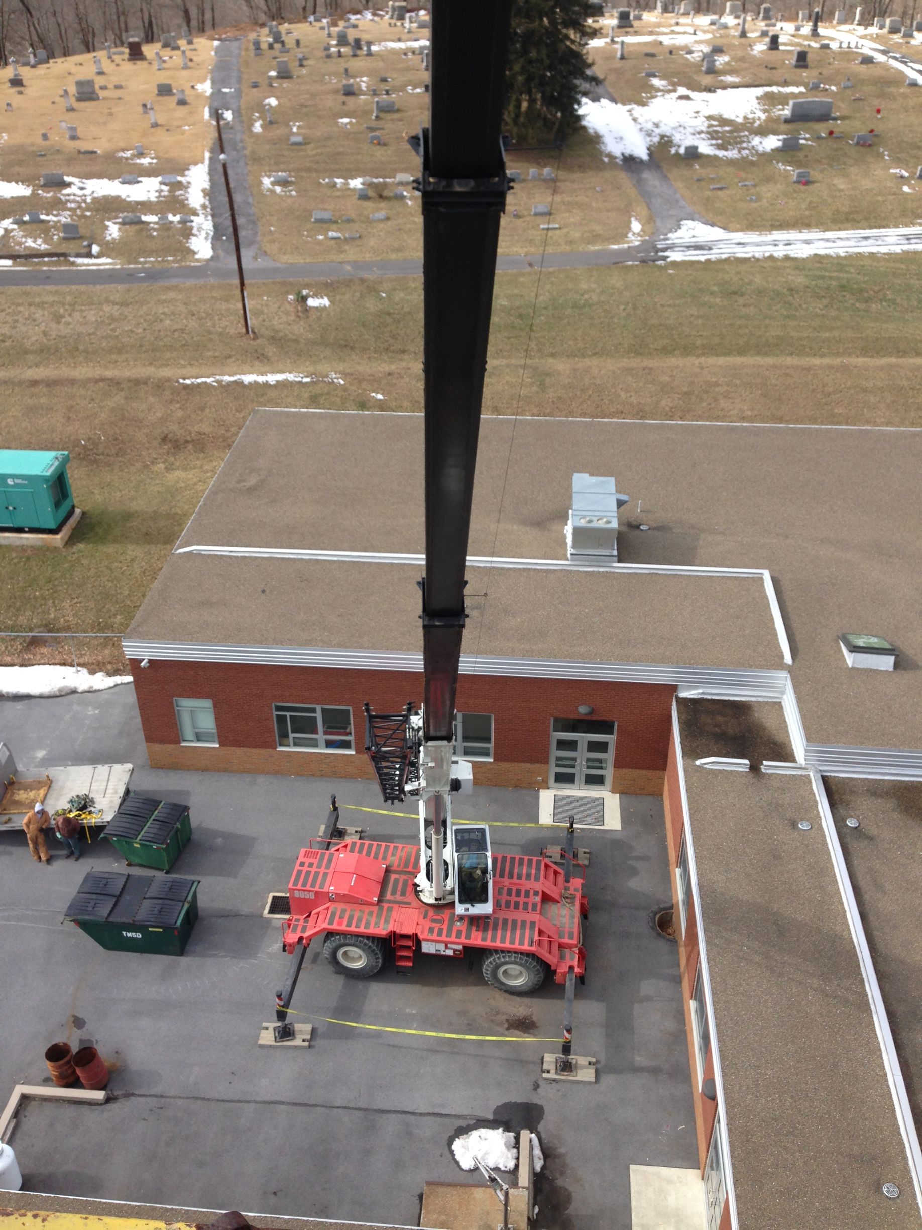 Crane lifting equipment beside a red brick building in a parking lot, aerial view