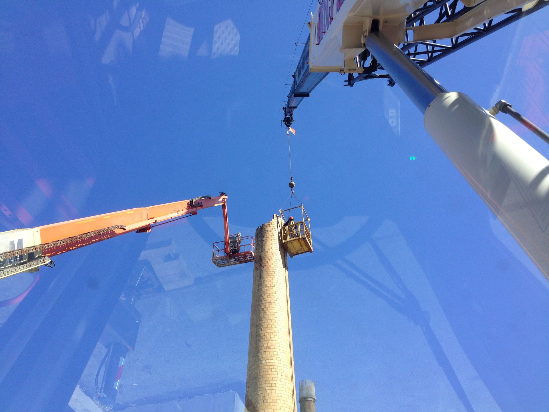 Two cranes lifting a tall concrete column against a blue sky
