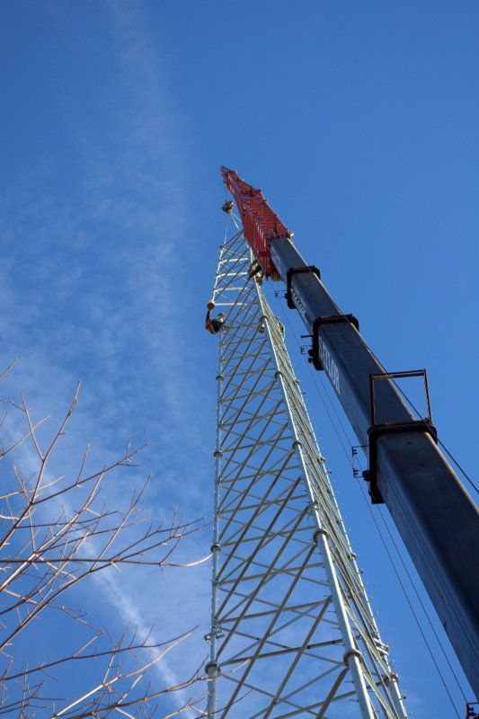Crane lifting a red-tipped lattice tower against a blue sky