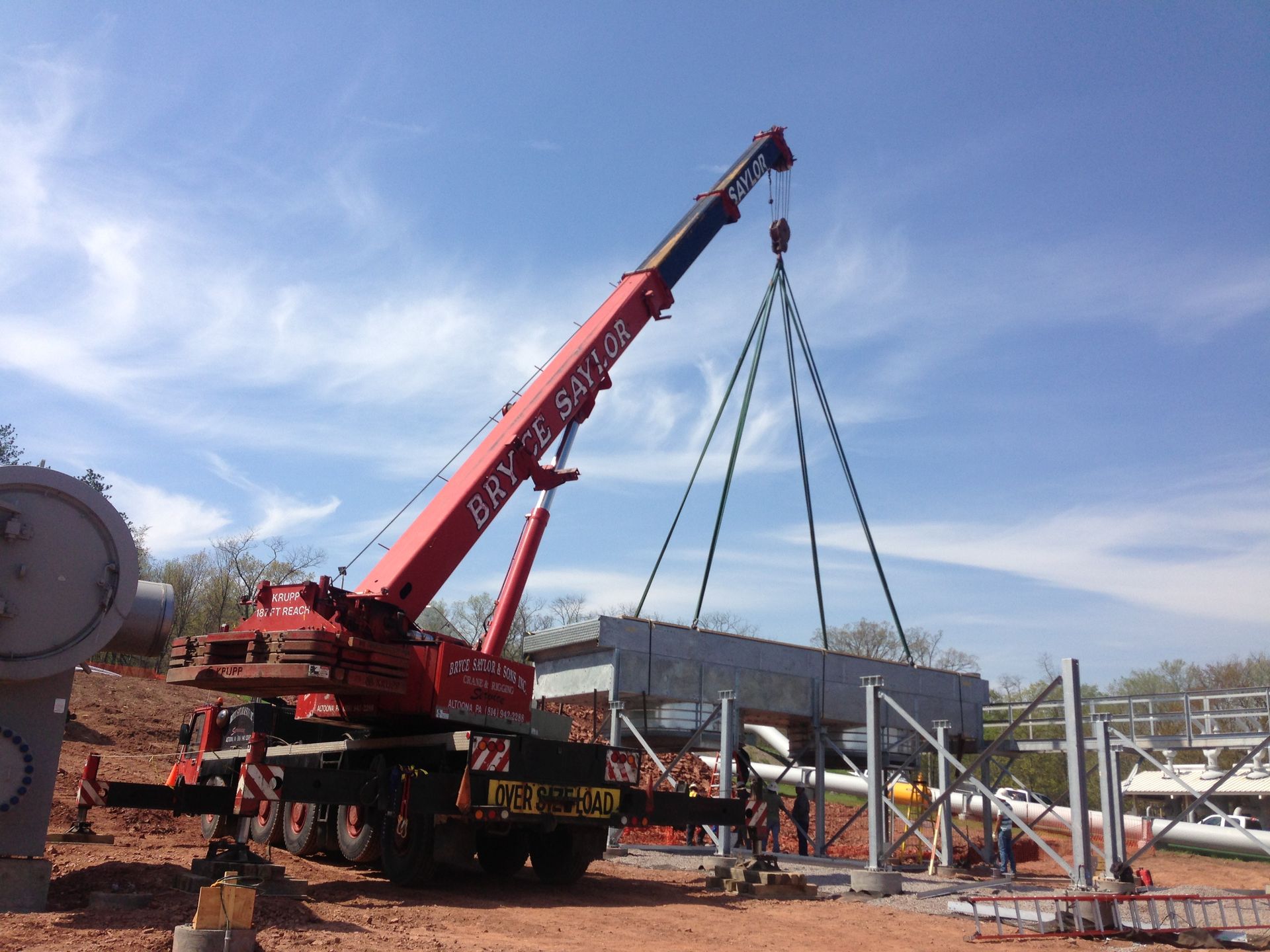 Red crane lifting a steel frame at an outdoor construction site under a blue sky
