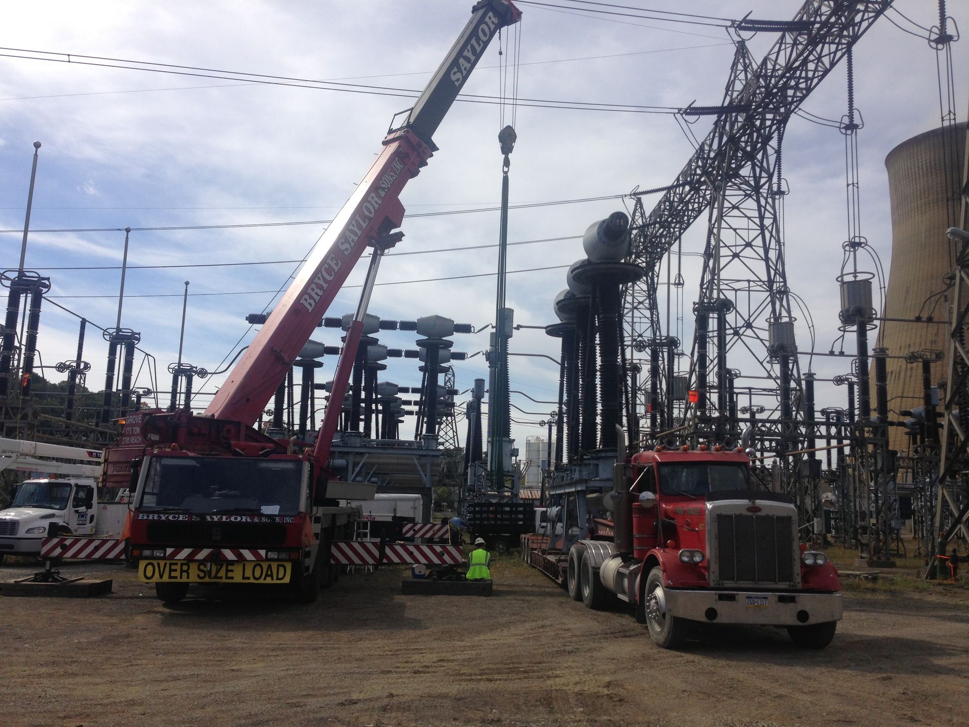 Crane and truck at an electrical substation, with workers lifting heavy equipment under power lines.