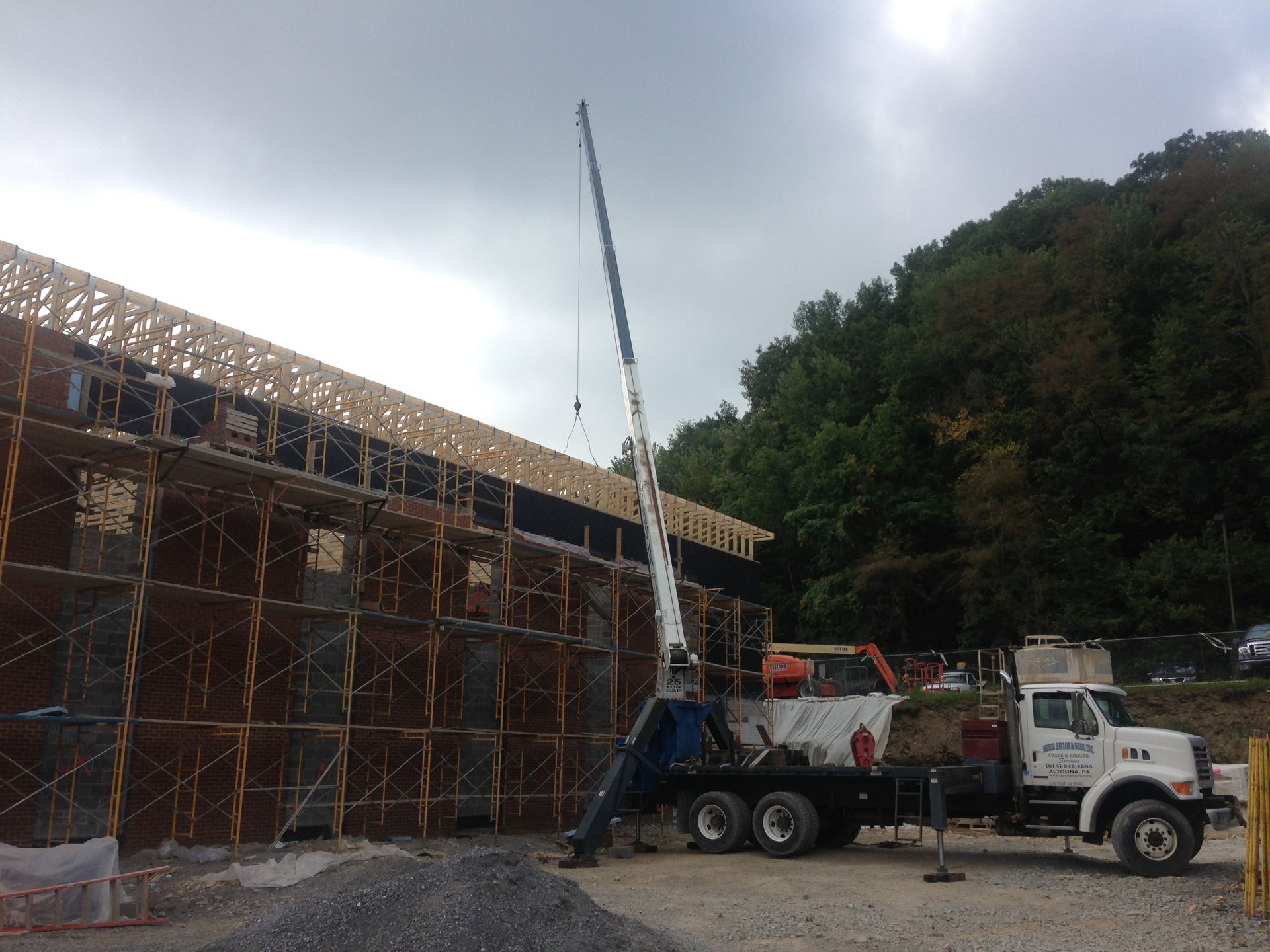 Truck-mounted crane lifting materials at a construction site beside a wooded hillside