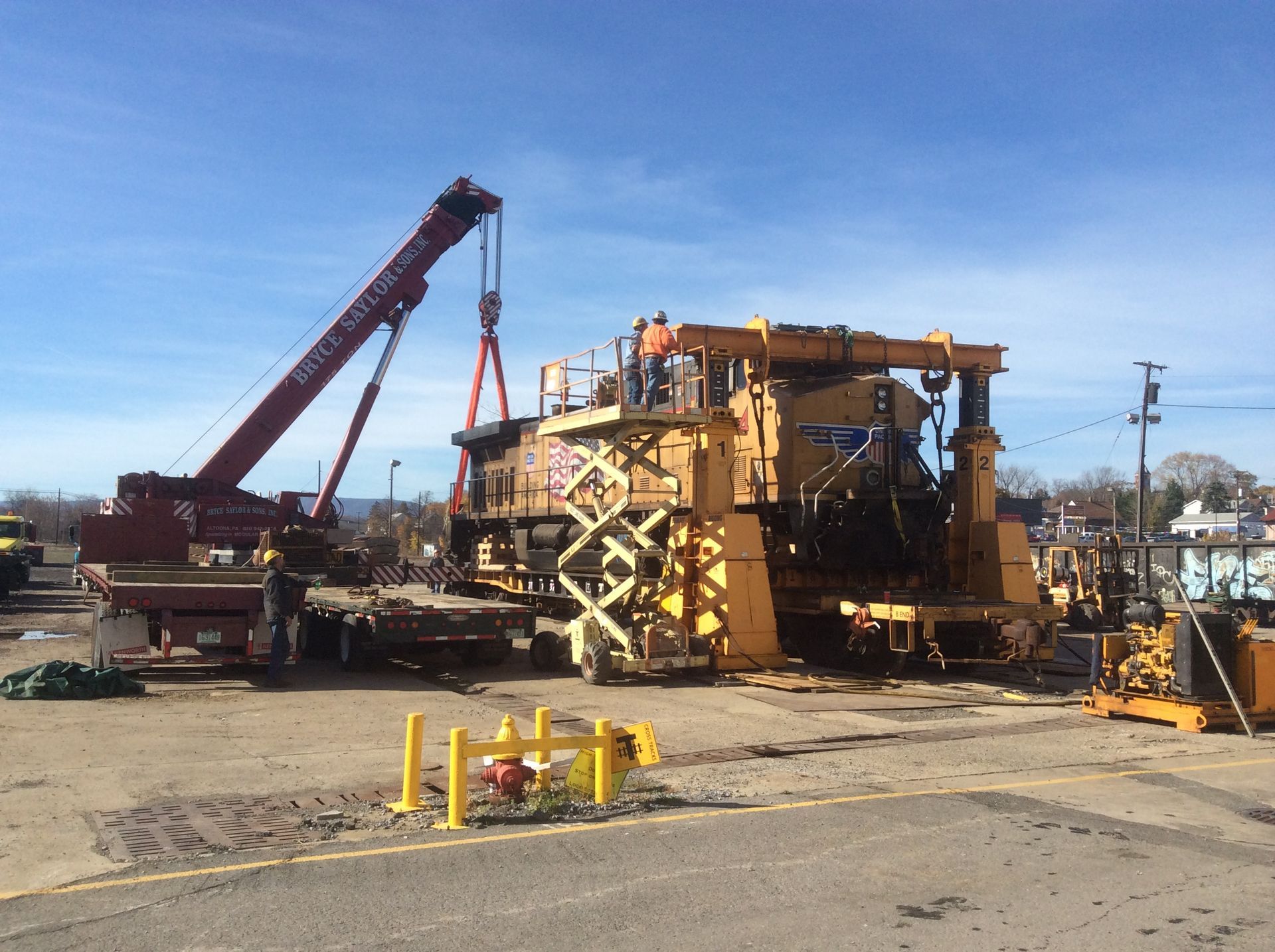 Workers and a crane beside a large yellow industrial machine at a construction site.
