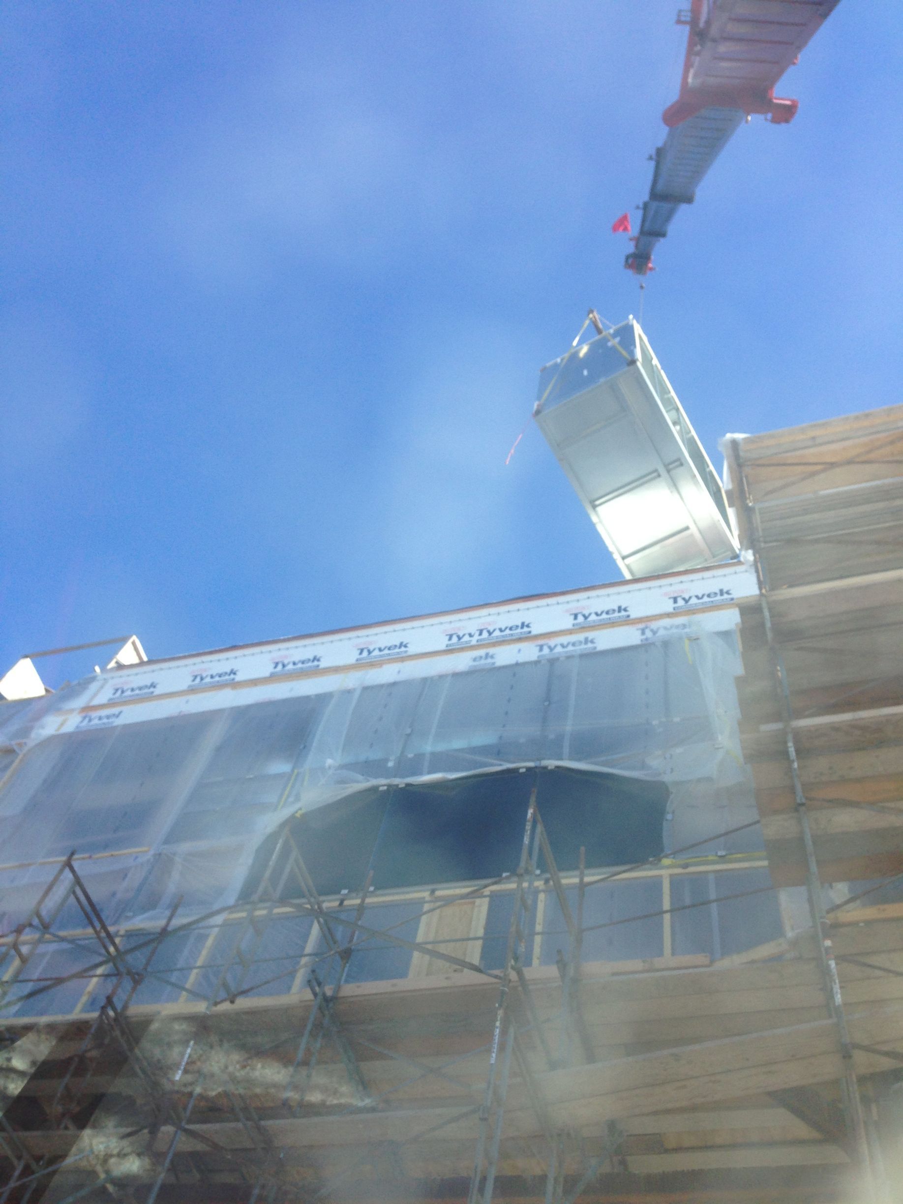 Scaffolding around a building under renovation, with blue sky and a metal lift overhead.