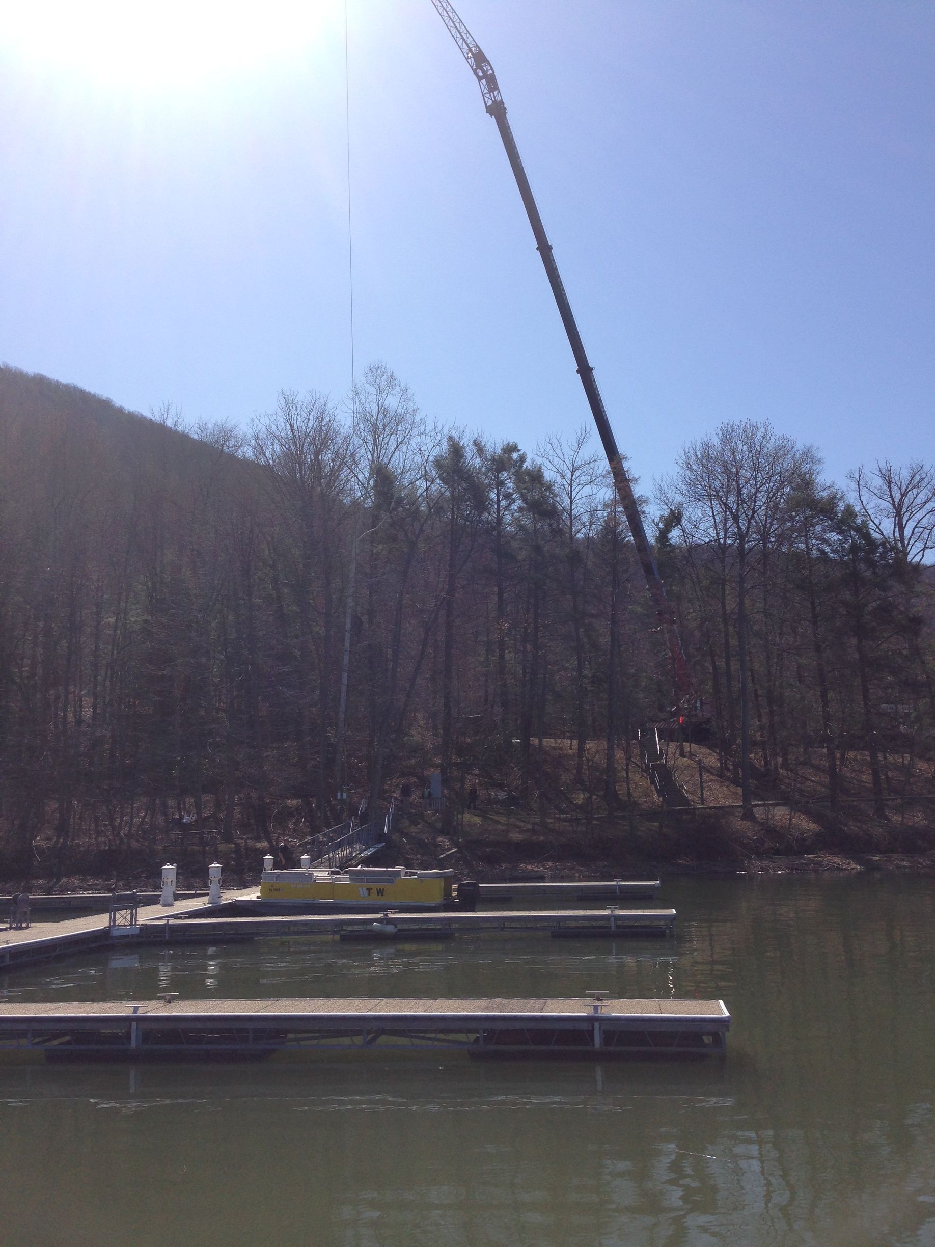 Floating docks on a calm lake beside a wooded hillside under a bright blue sky.