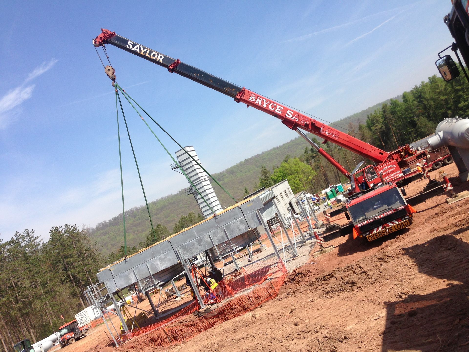 Red crane lifting steel beams at a construction site under a blue sky