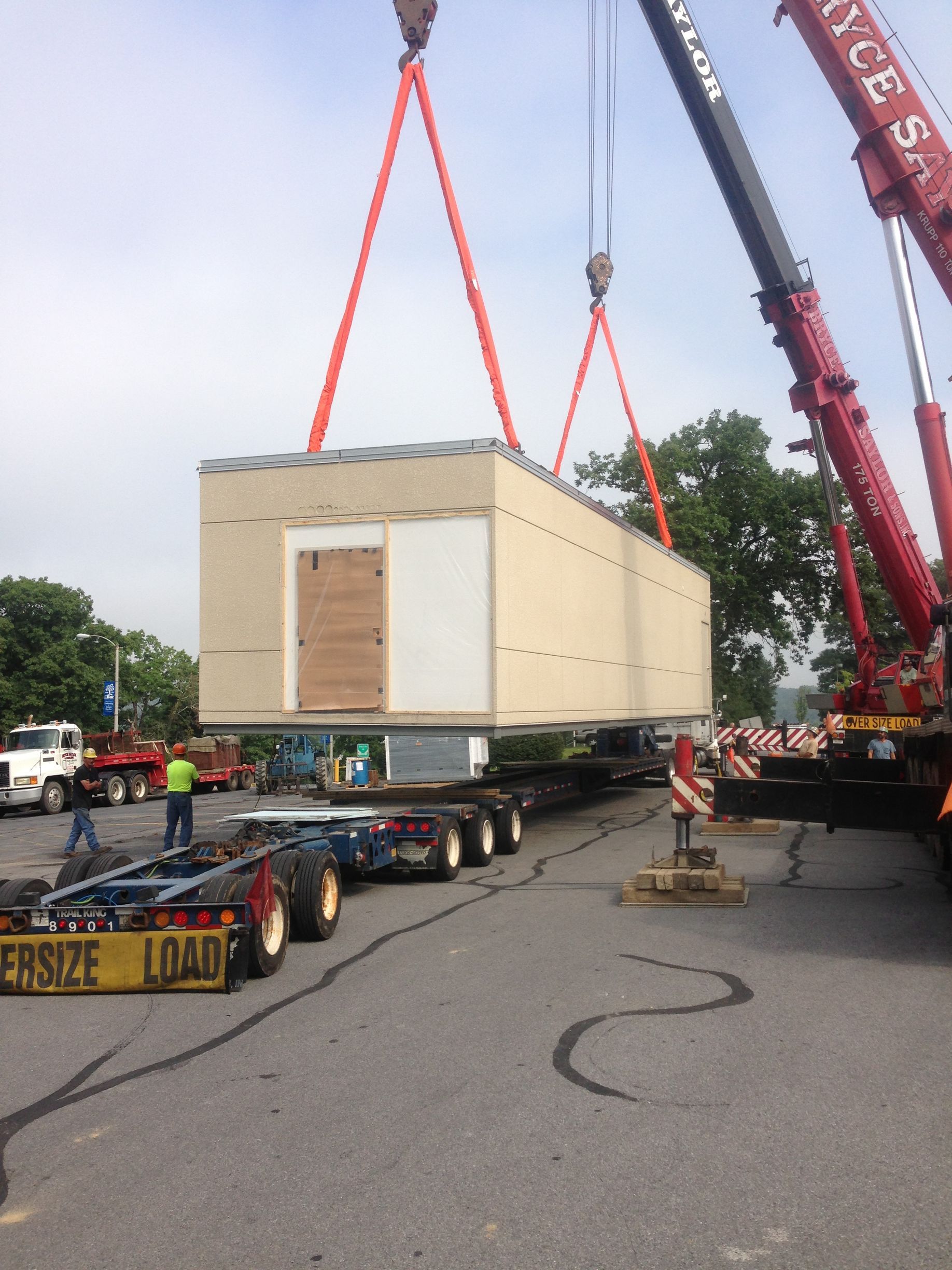 Large crate being lifted by cranes onto a heavy transport truck at a roadside site