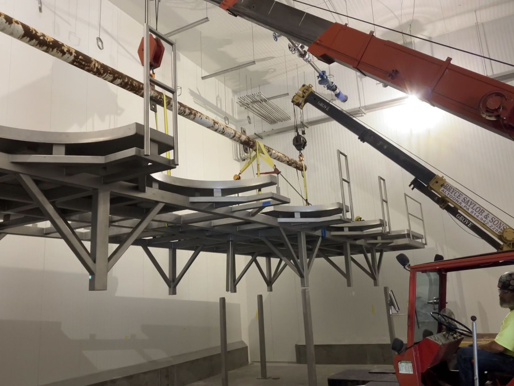 Construction site with workers on elevated metal platforms and booms inside a large indoor space