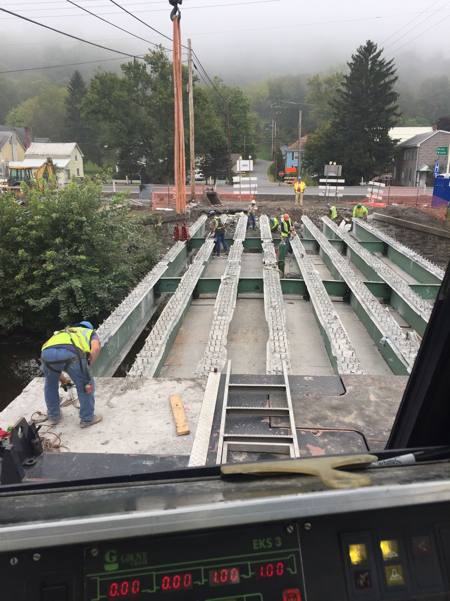 Construction site with concrete beams, a worker in a yellow jacket, and a crane in rainy conditions.
