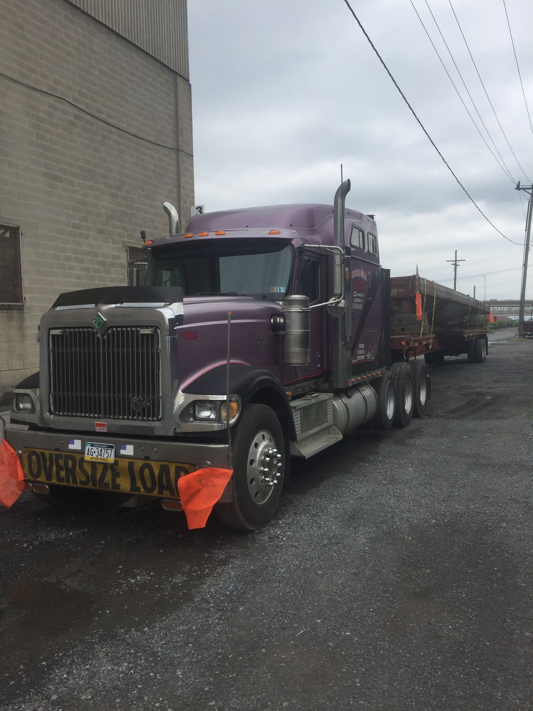 Purple semi truck parked on a wet street beside a building, with orange flags on the front.