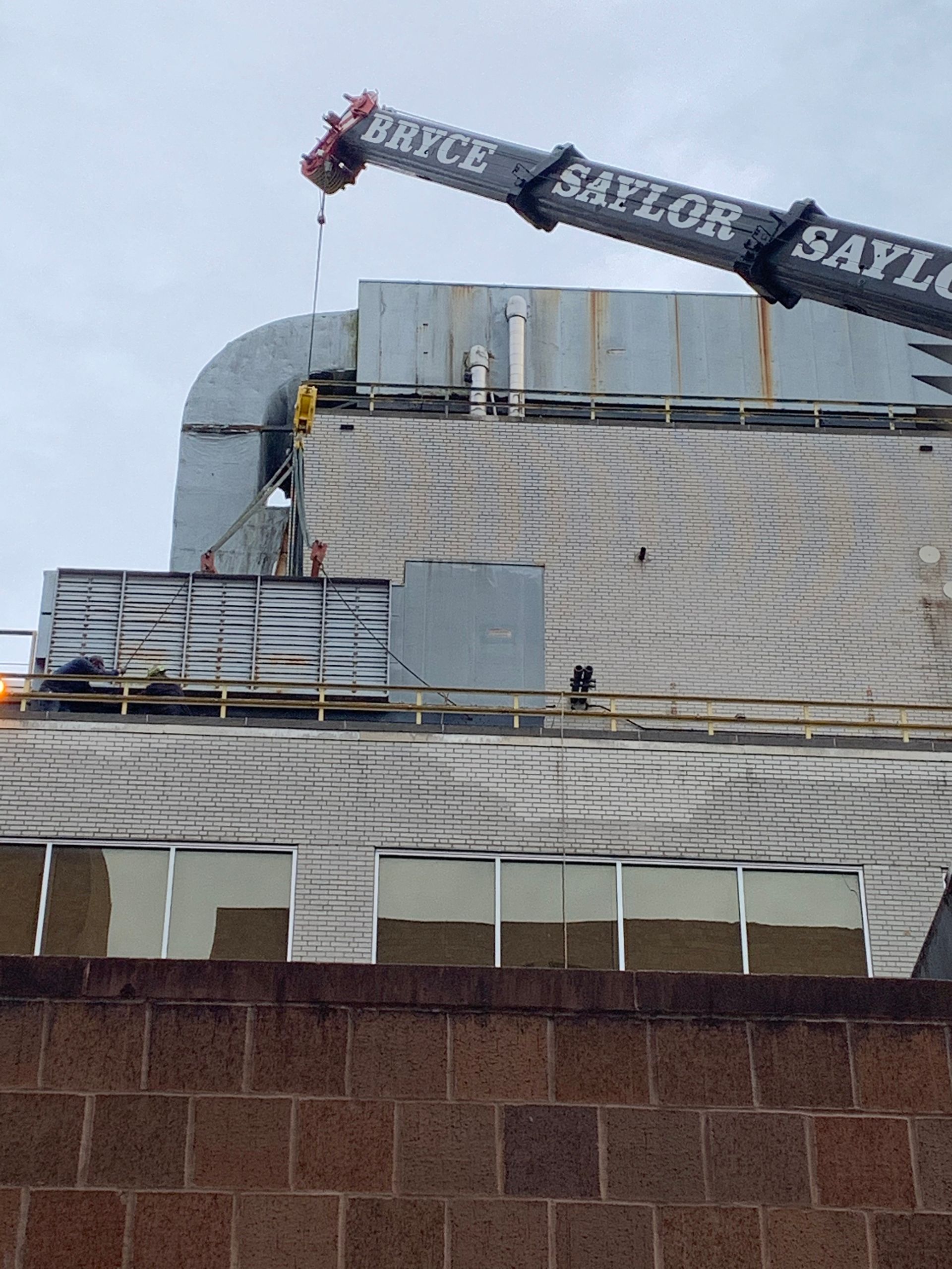 Crane arm over a building rooftop with stacked materials and siding panels under a cloudy sky