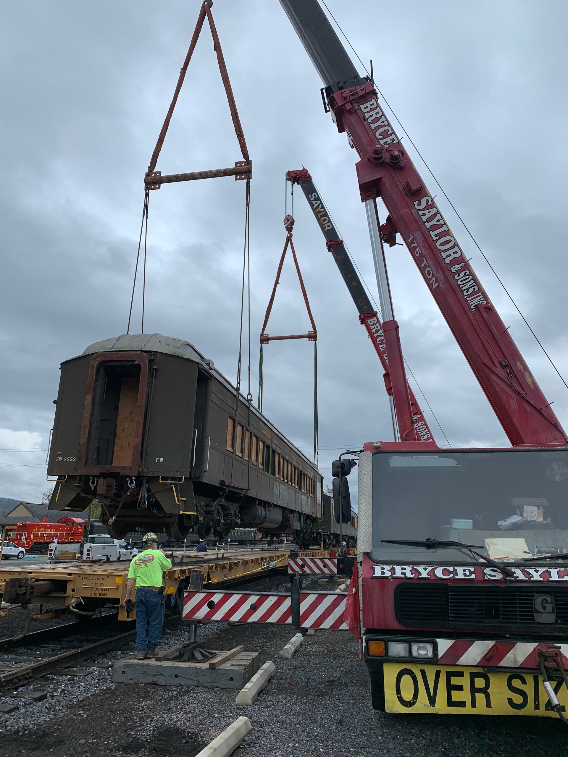 Heavy crane lifting a derailed railcar beside emergency vehicles and workers on a roadway