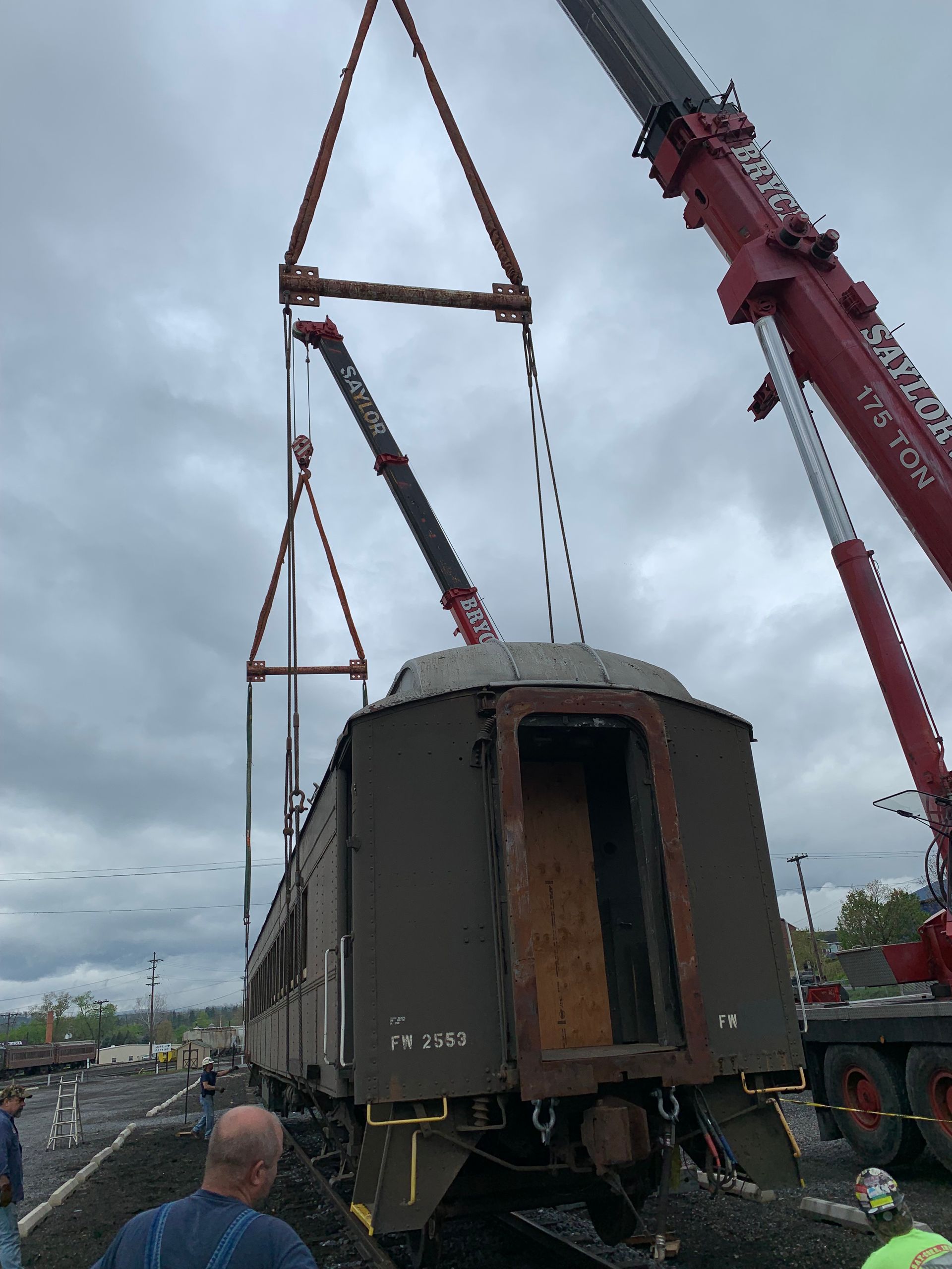 Crane lifting a weathered railcar onto a flatbed truck in a work yard.