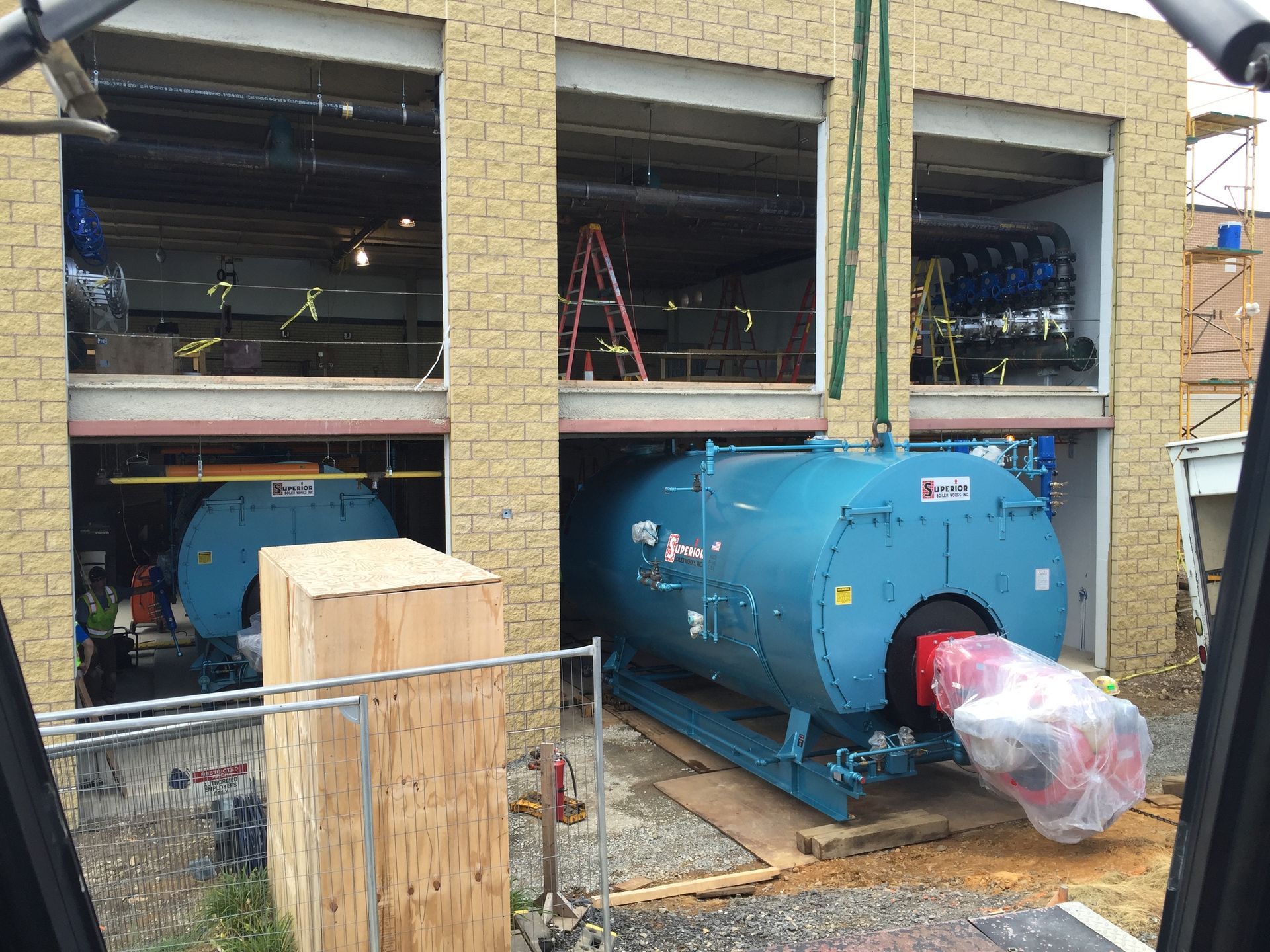 Large blue industrial machine outside a brick building, with equipment visible through open wall bays.
