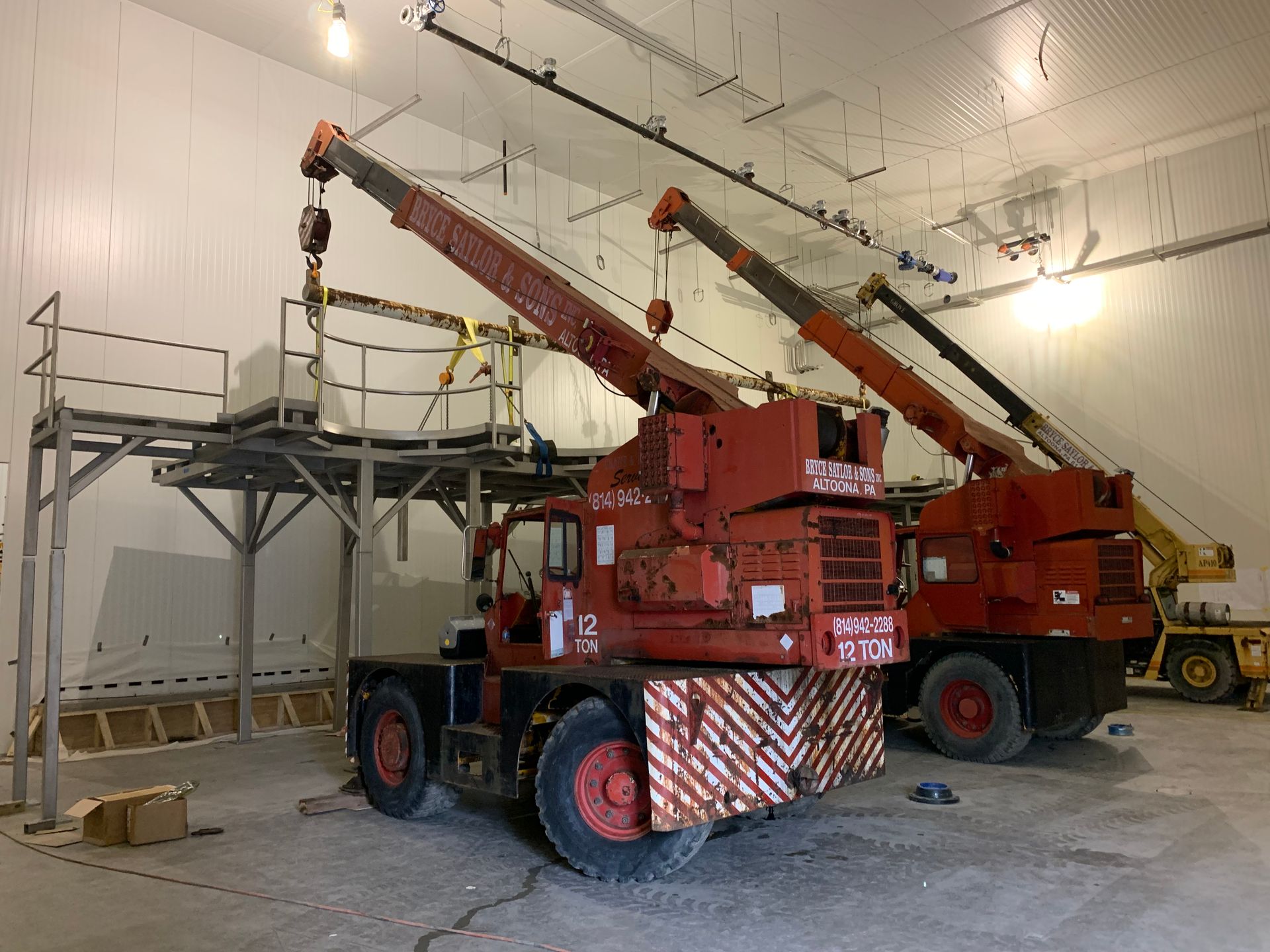 Two red industrial cranes inside a warehouse, with raised booms and a metal platform on the left