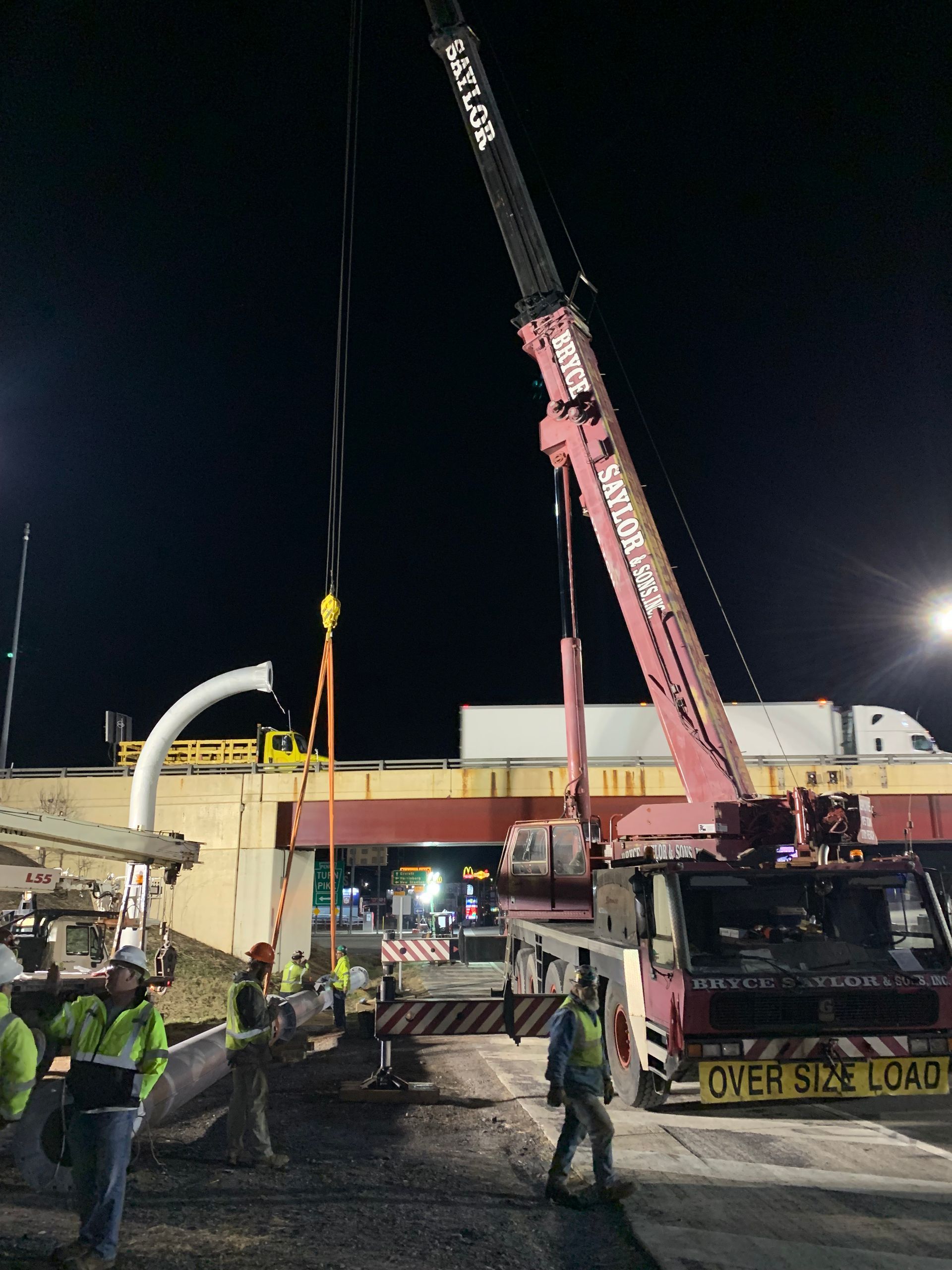 Nighttime construction site with crane lifting equipment and workers in high-visibility vests