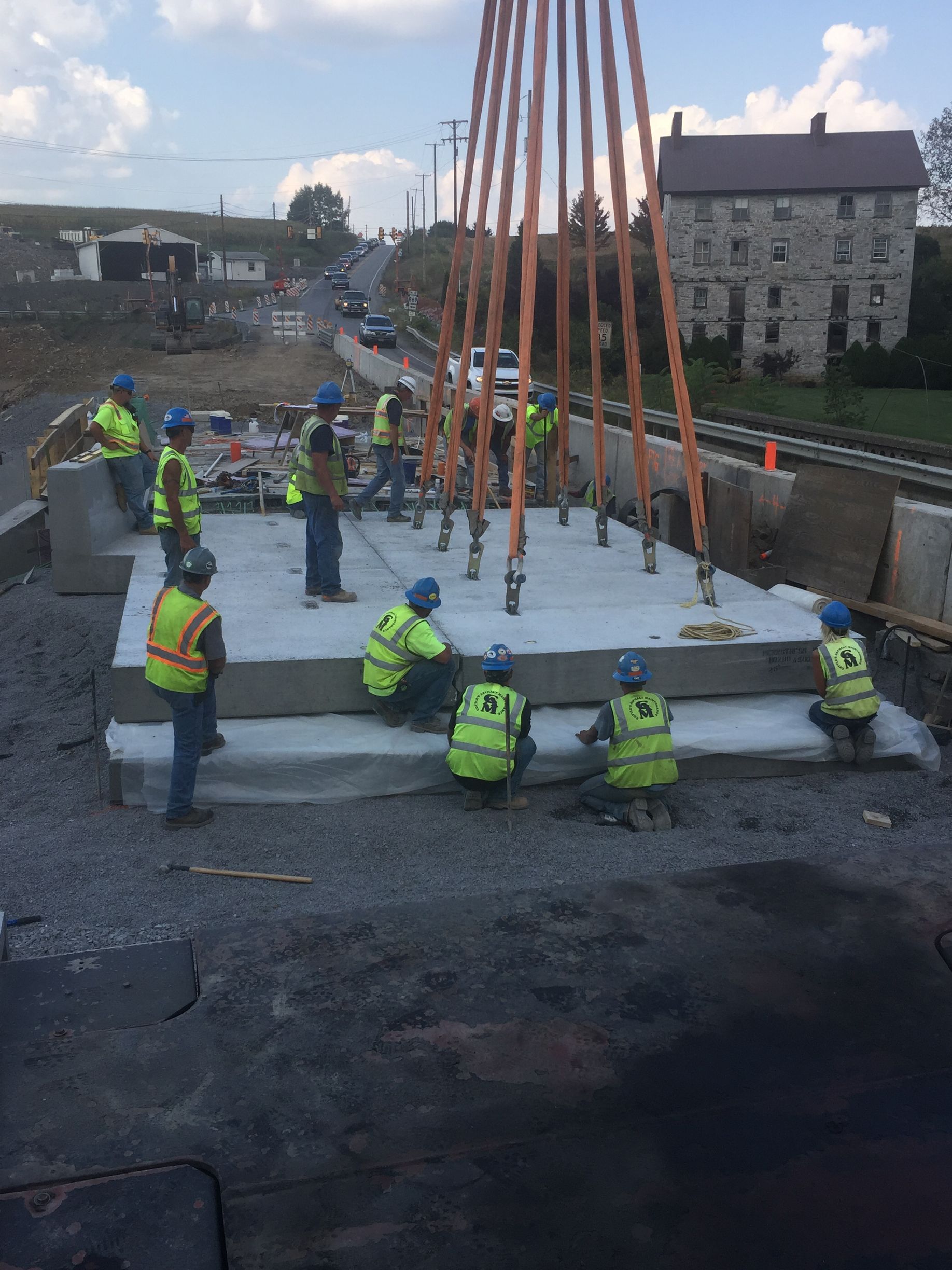 Workers in high-visibility vests pour concrete at a construction site with cranes and scaffolding.