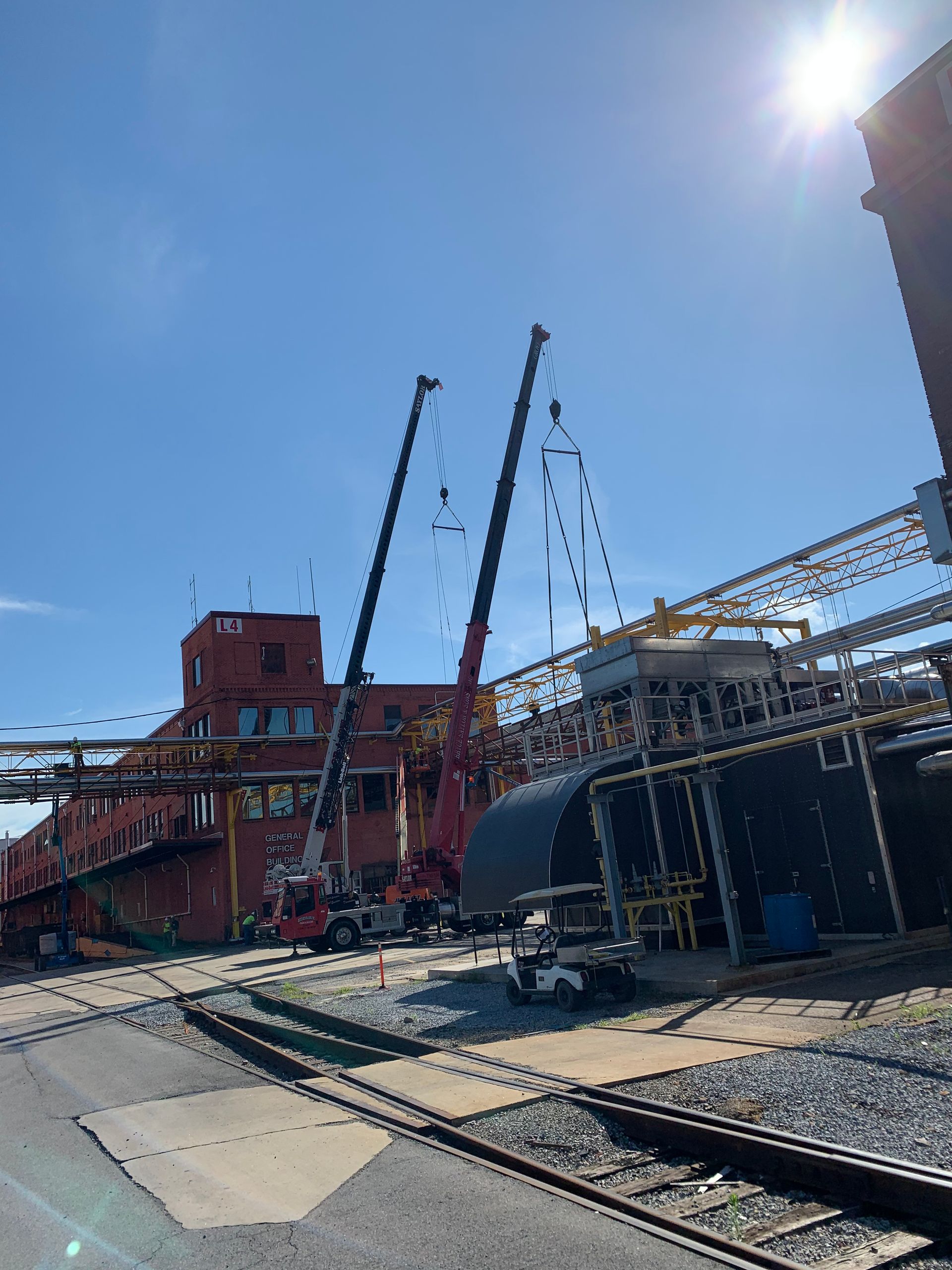 Industrial harbor with cranes, docked ship, and rail tracks under a bright sun.