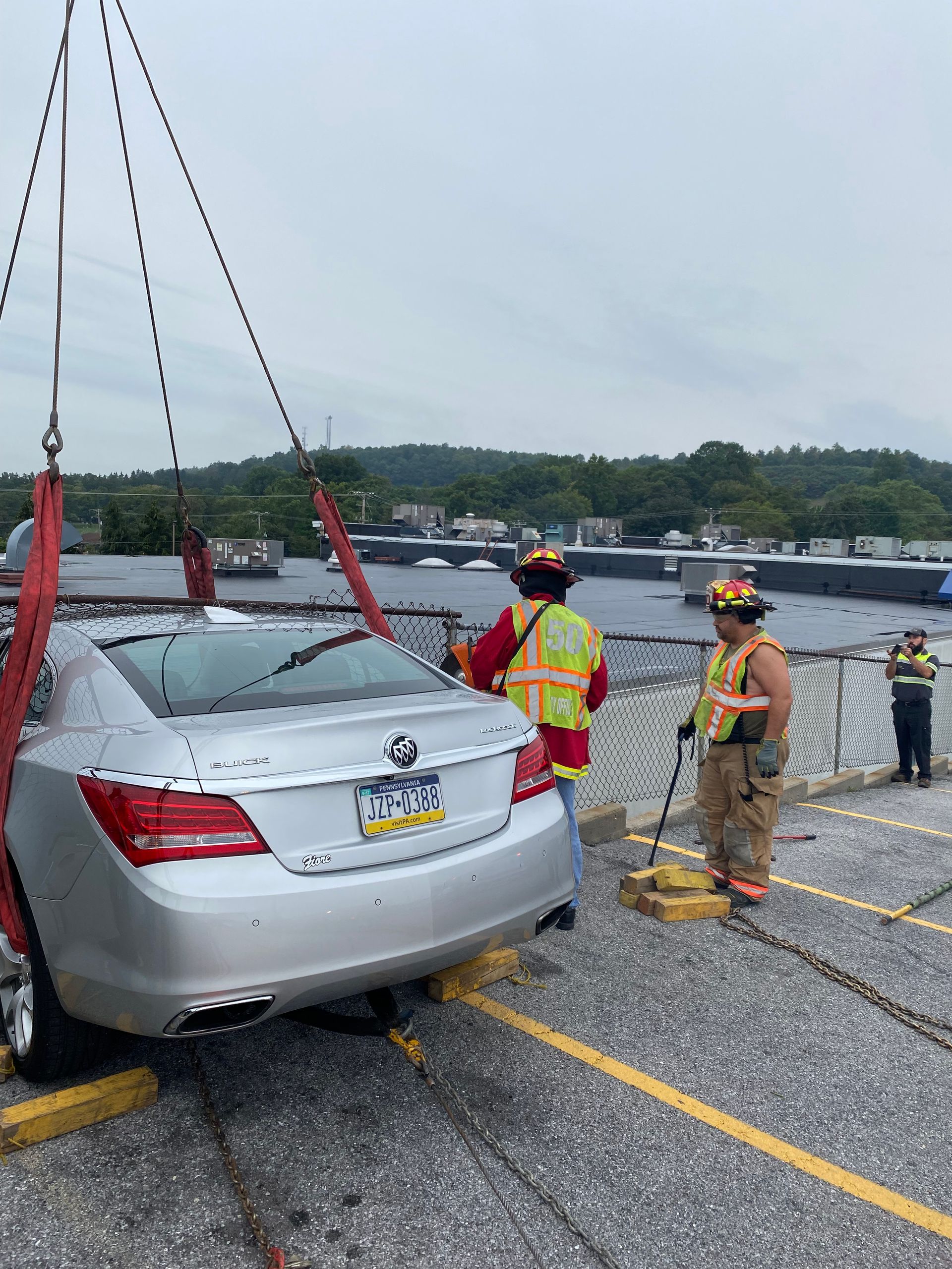 Tow truck lifts silver sedan from flooded parking lot as workers in safety gear stand nearby