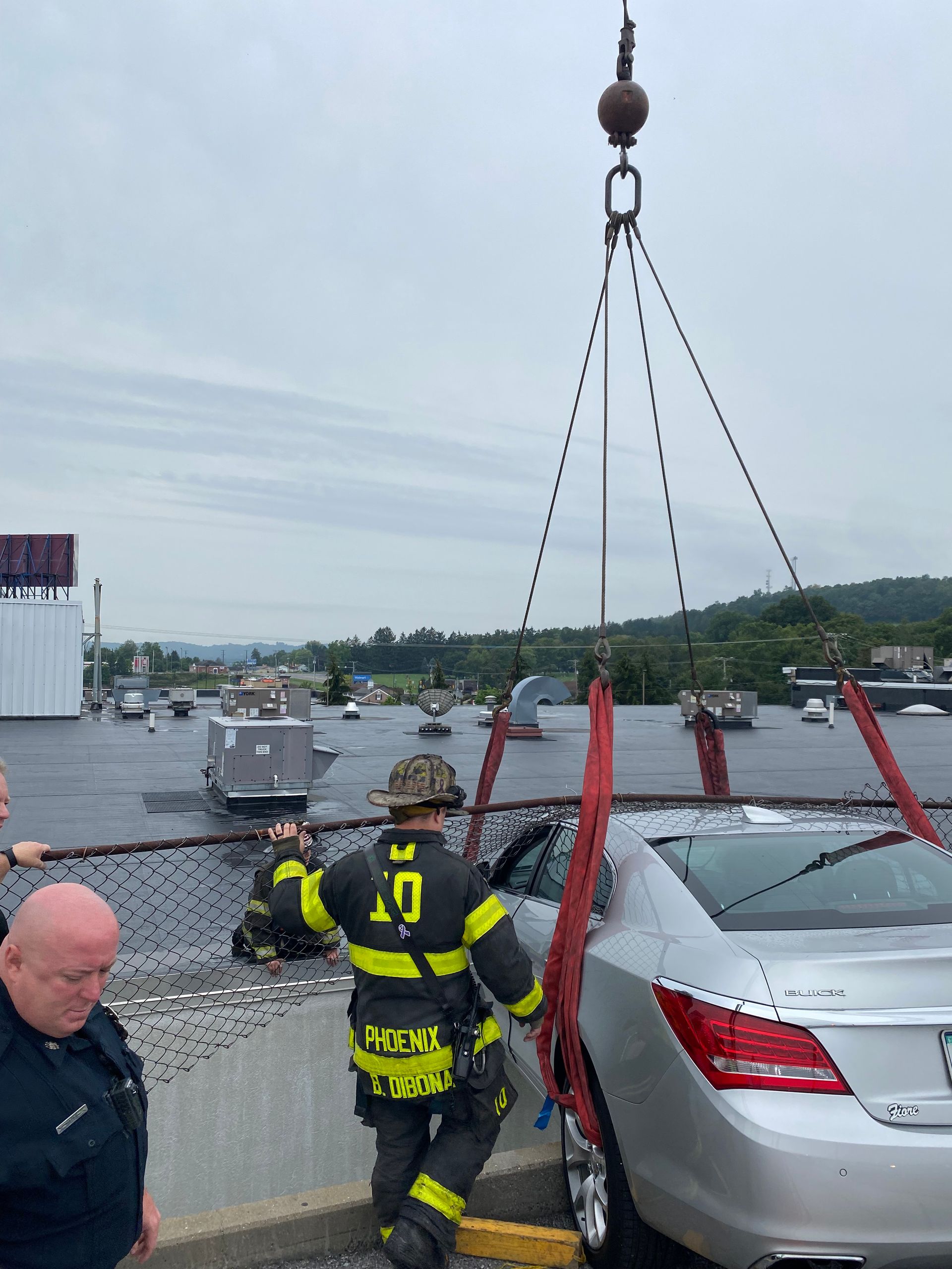 Tow truck lifts a silver car while firefighters stand nearby in a flooded parking lot