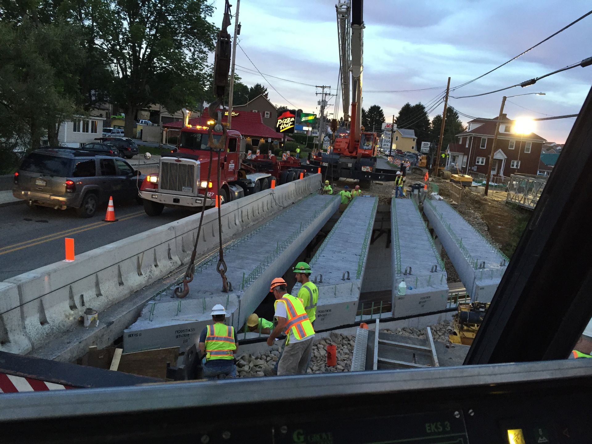Utility workers repair a road trench with concrete barriers and heavy machinery at dusk