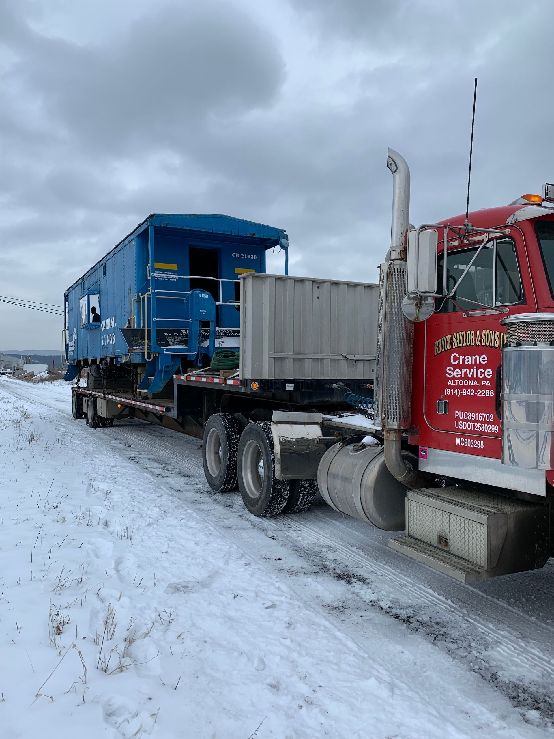 Blue and red truck hauling a blue dumpster on a snowy road under overcast skies