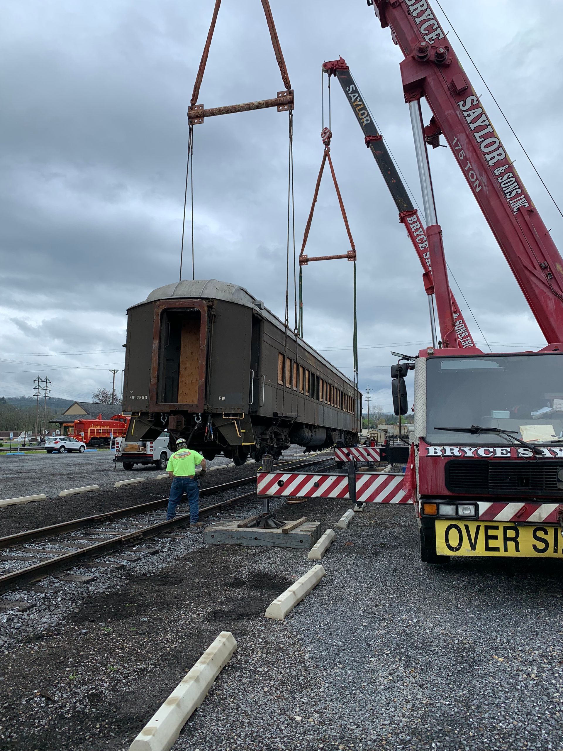 Crane lifting a damaged train car at a muddy rail work site under gray skies.