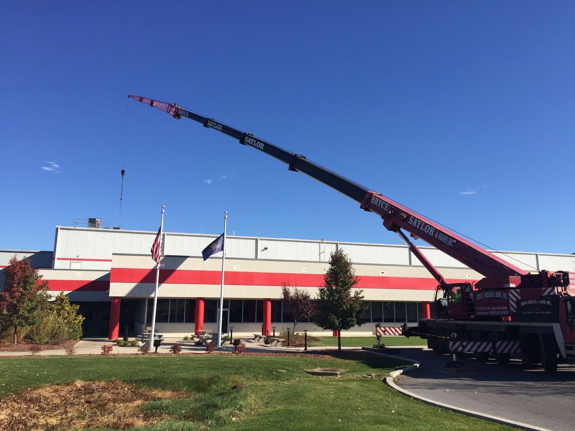 Large crane beside a red-and-white building with flags under a clear blue sky