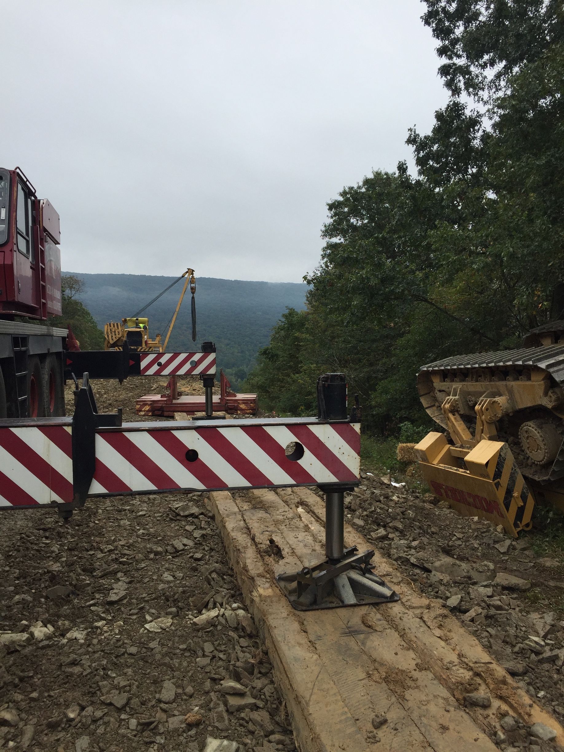 Construction site with striped barriers, a bulldozer, and a muddy road by a wooded hillside